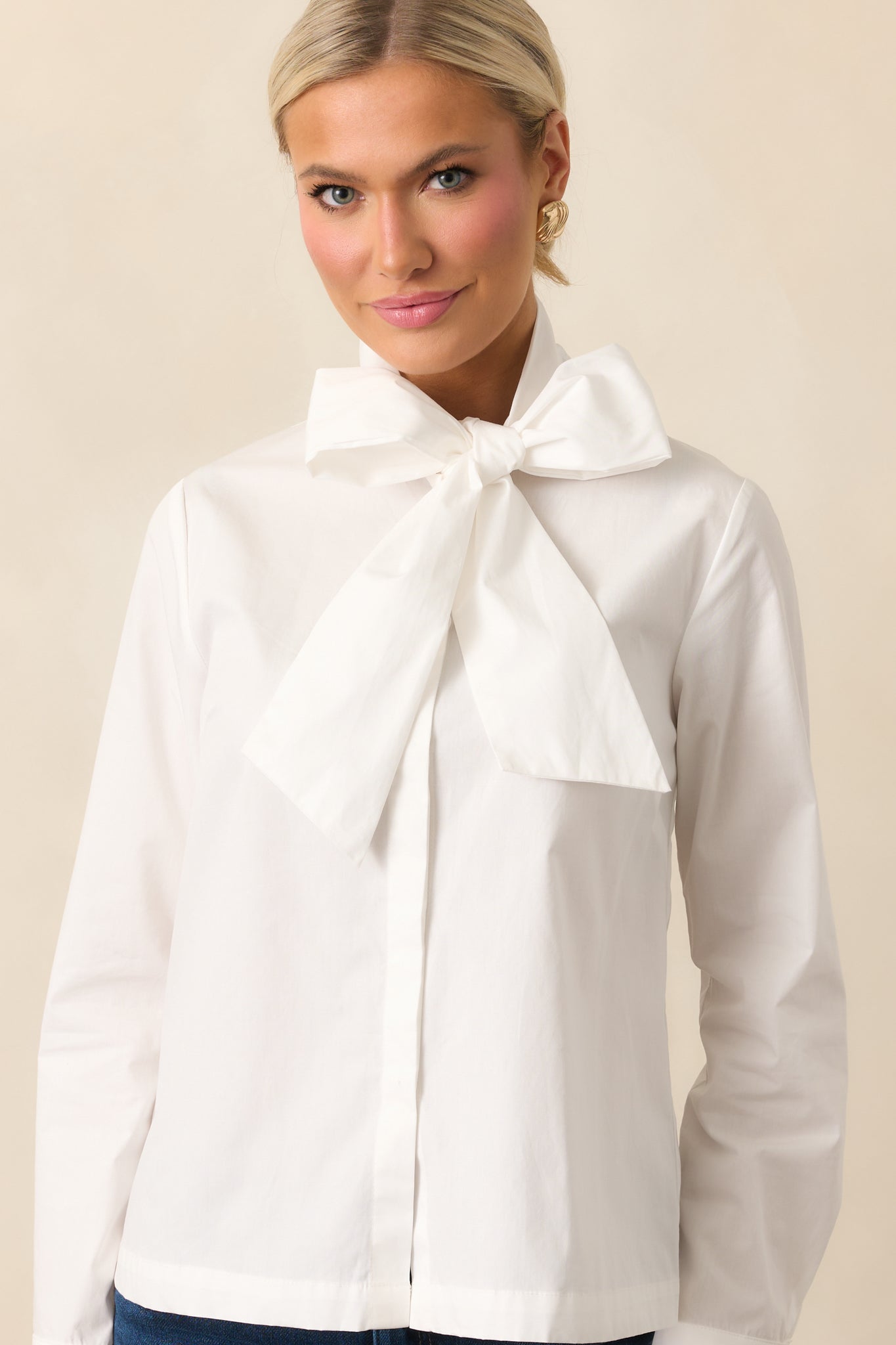 White top with a self-tie bow neckline and long sleeves with button cuffs.