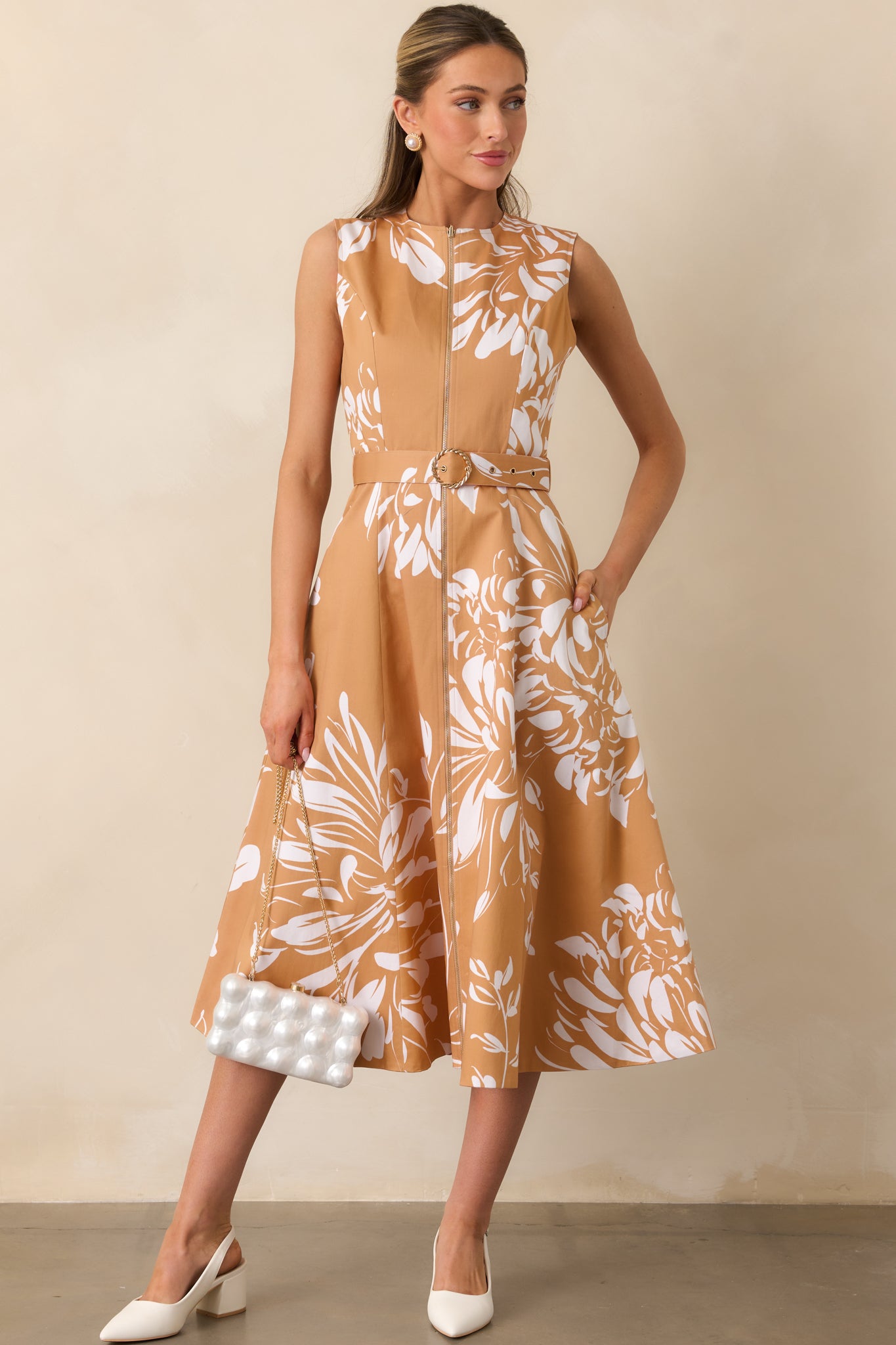 Sleeveless midi dress featuring fawn brown fabric with ivory floral print, round neckline, and gold front zipper.