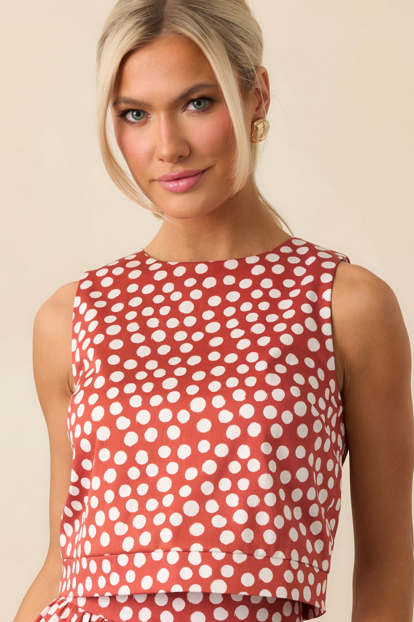 Close view of the sleeveless cut and crew neckline of the brick red polka dot top.