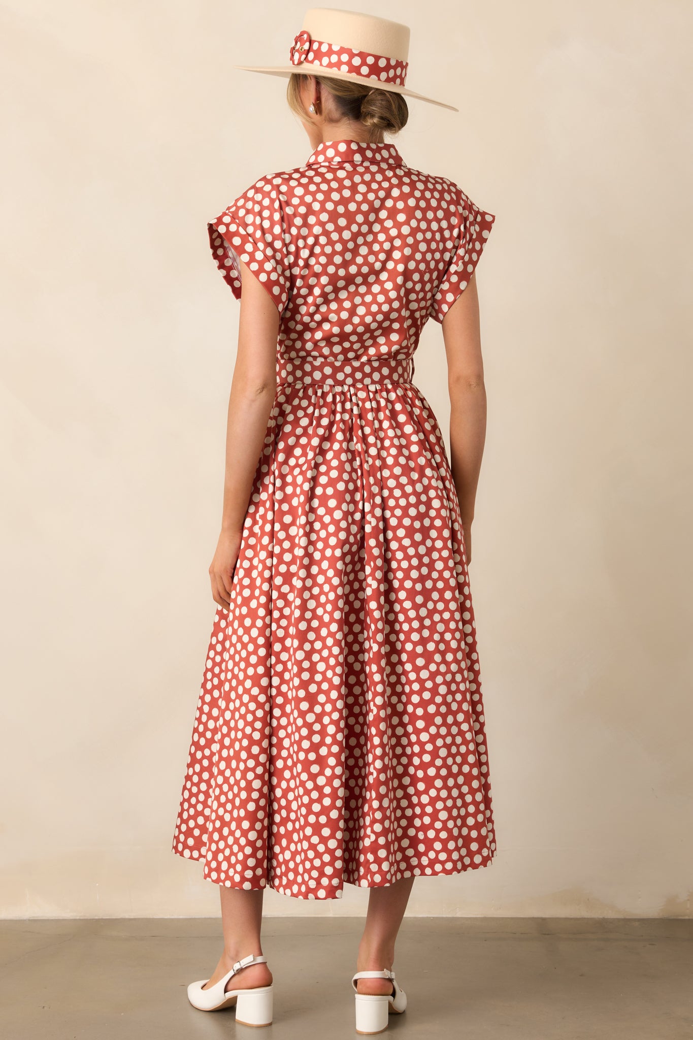 Rear view of the brick red maxi dress with ivory polka dots, showing cuffed sleeves and flowing silhouette.
