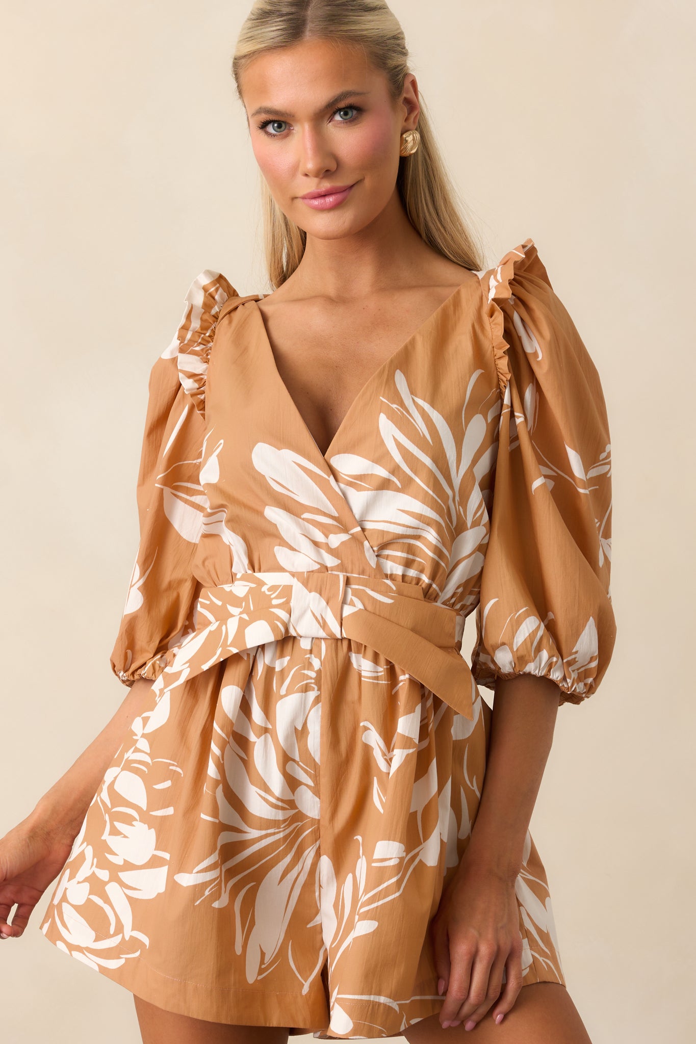 Cropped view highlighting the floral print, elastic sleeve cuffs, and ruffle shoulder trim on the fawn brown romper.