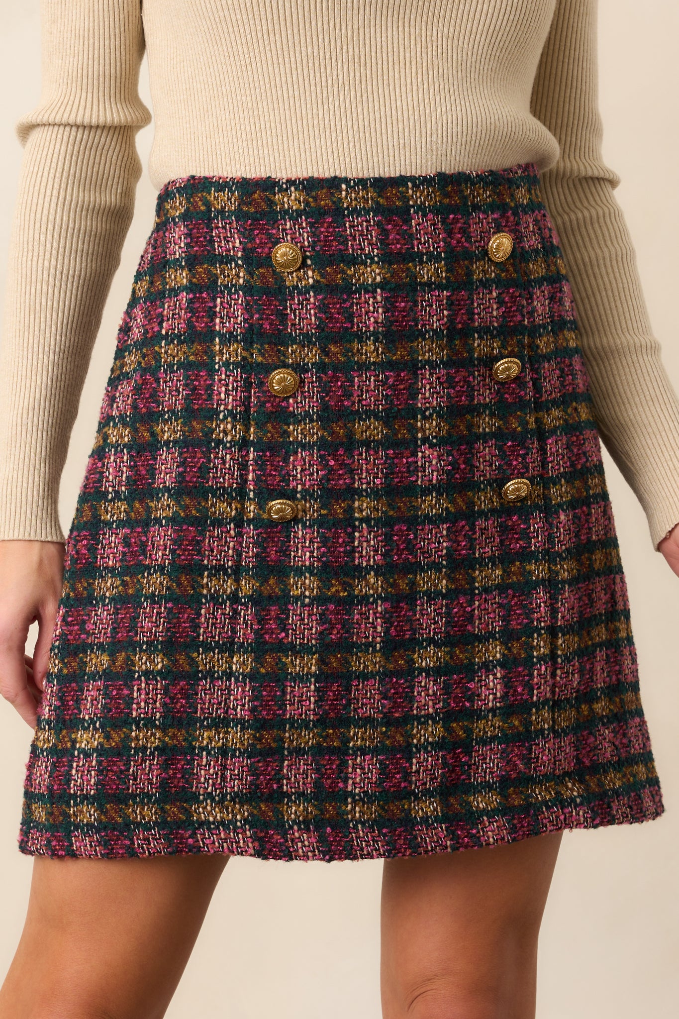 Close view of the gold crest-style buttons and plaid tweed pattern on the mini skirt.