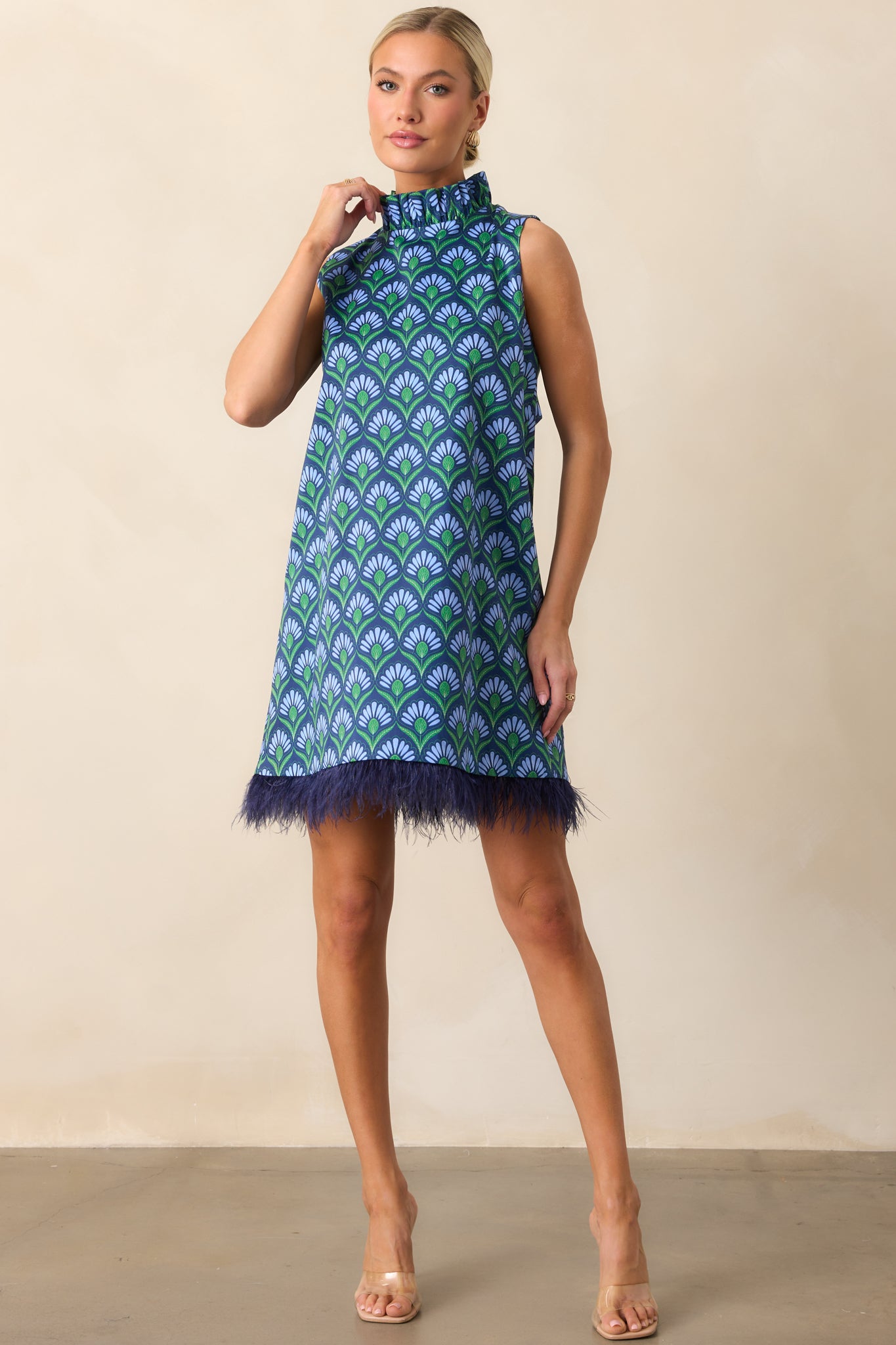 Mini dress featuring functional pockets, a high ruffled mock neckline, and playful blue feather trim at the bottom.