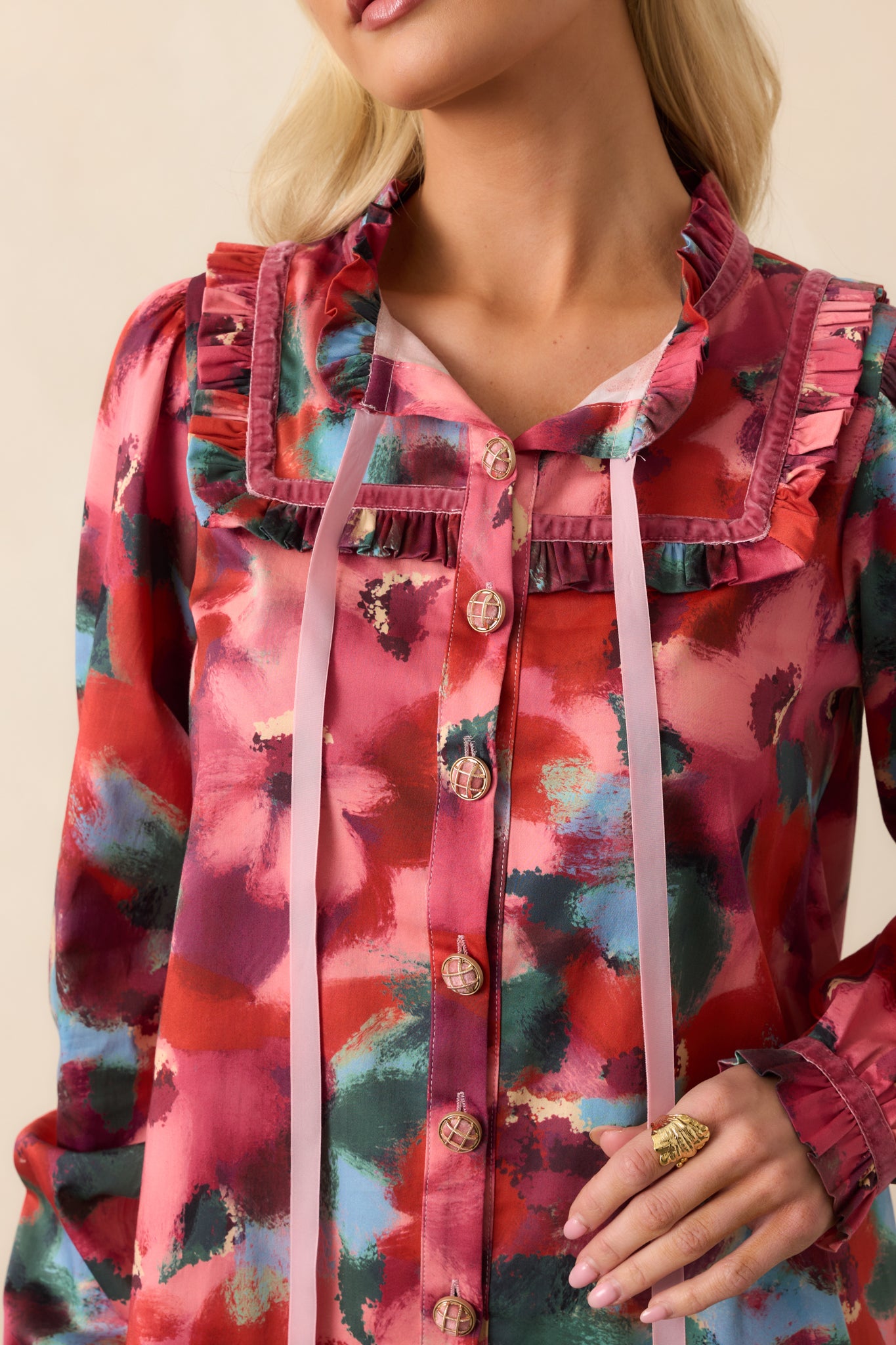 Extreme close-up of the pink top showing the multicolor abstract floral print, ruffle-trimmed collar, and tied ribbon tassels at the V-neck.