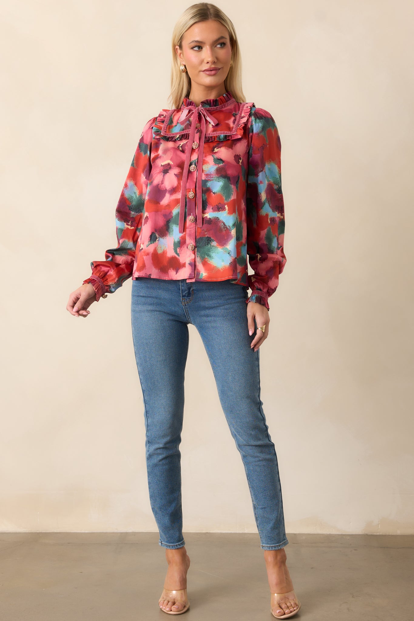 Pink floral top shown straight on, featuring a button-front closure, V-neckline with tassel ribbons, and puffed long sleeves ending in ruffled cuffs.
