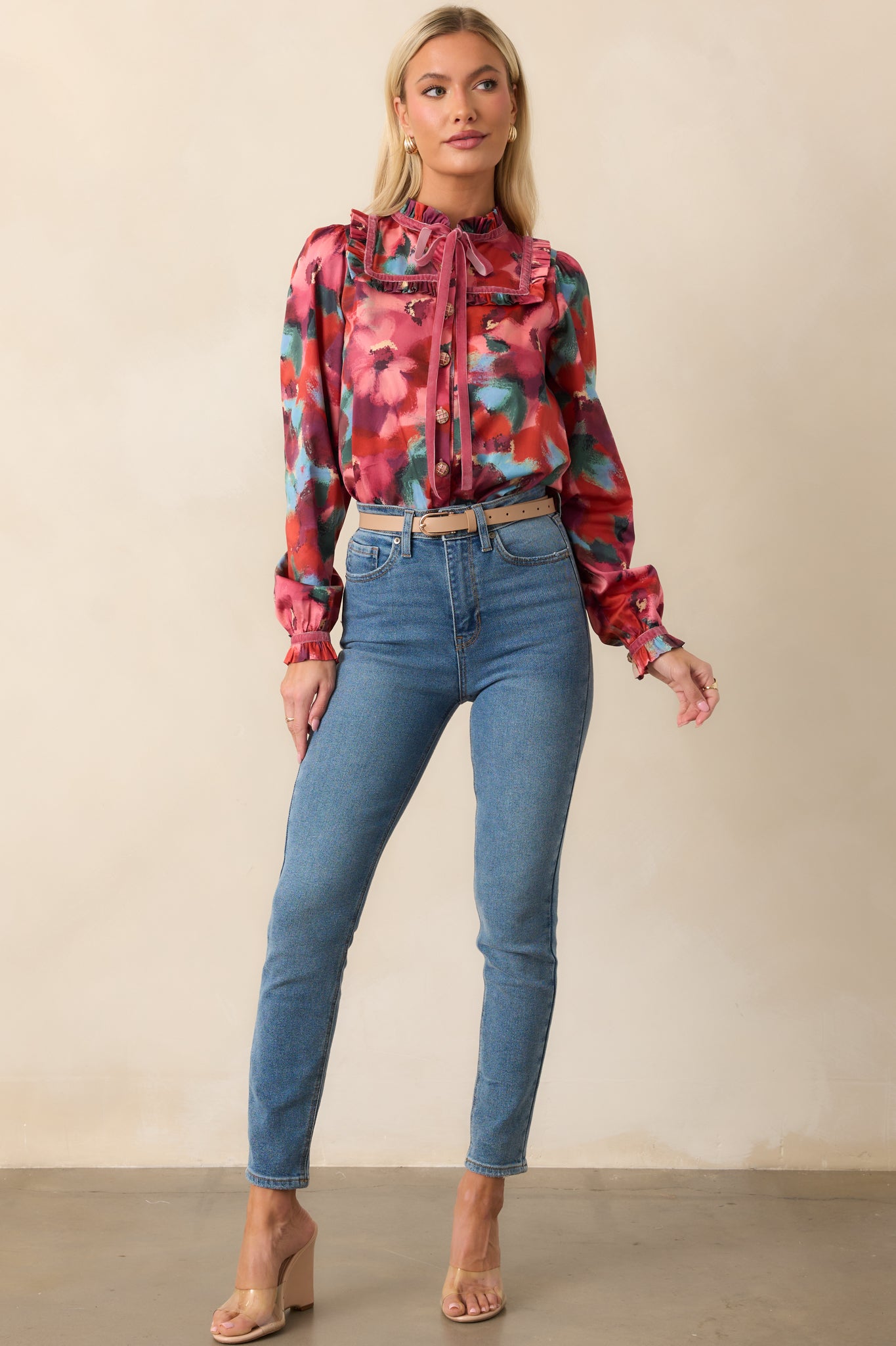 Front view of a pink top with multicolor abstract floral print, featuring a V-neckline with long ribbon tassels, button-front closure, and long puff sleeves with ruffled cuffs.