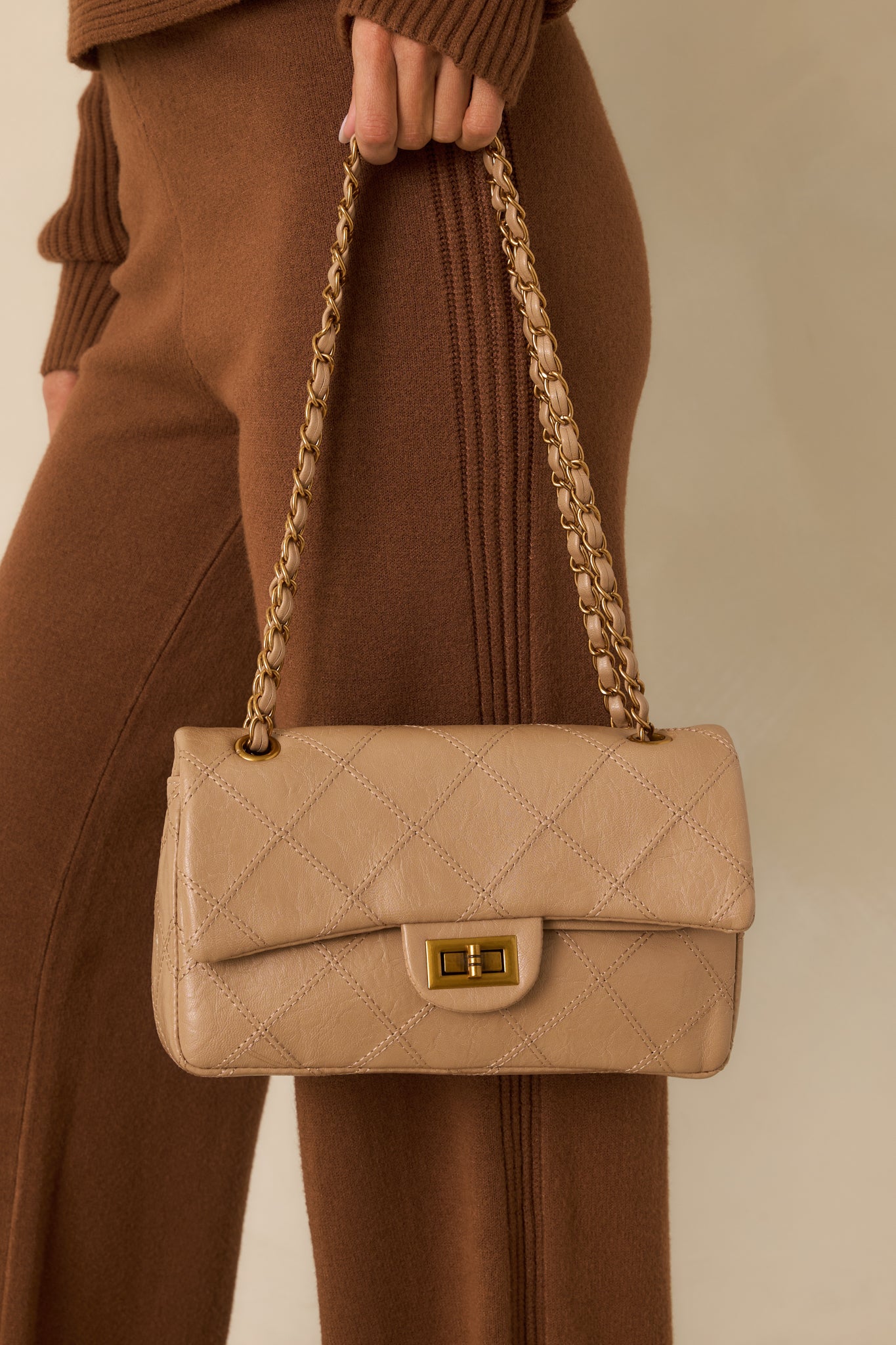 Quilted beige faux leather handbag featuring a gold-tone turn-lock closure and woven chain strap.