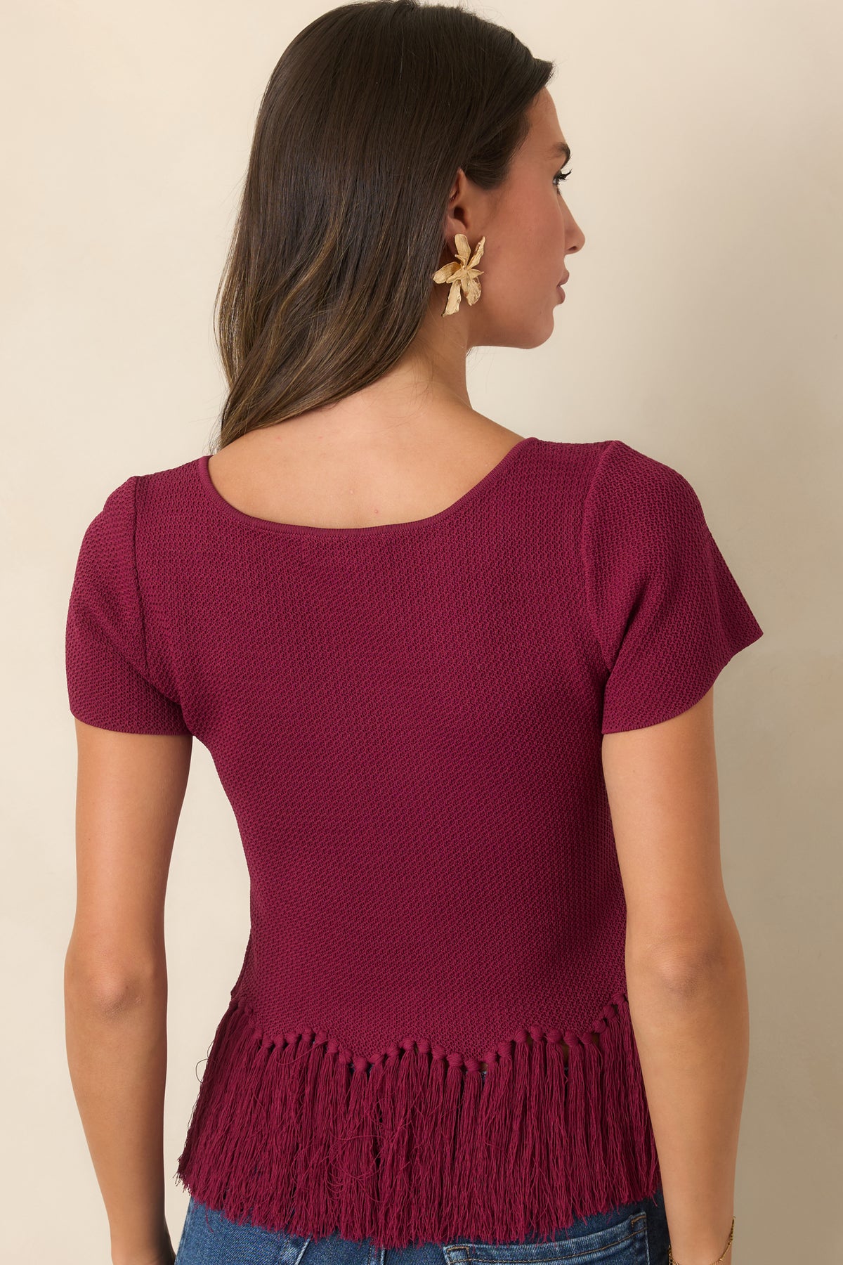 Rear view of the berry textured knit top with short sleeves and a fringe-trimmed hem.