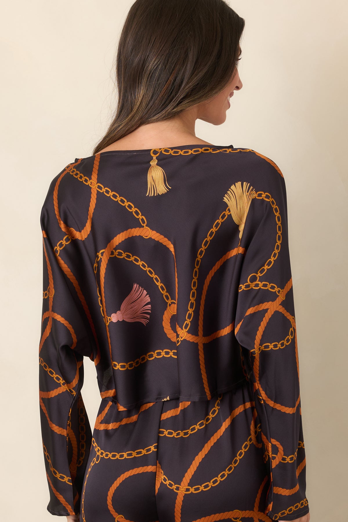 Rear of the black satin-feel cropped top featuring the looping rust rope and golden chain print with long sleeves and a relaxed fit.