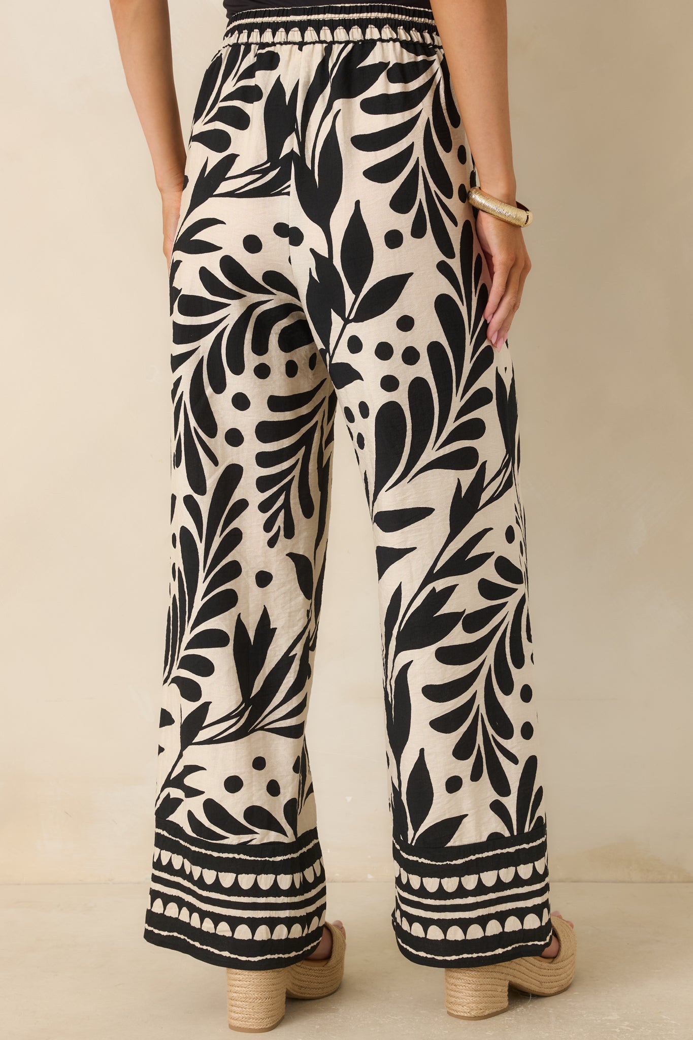 Rear view of relaxed wide-leg pants featuring a flowing silhouette, elastic waistband, and bold botanical print with border hem detail.
