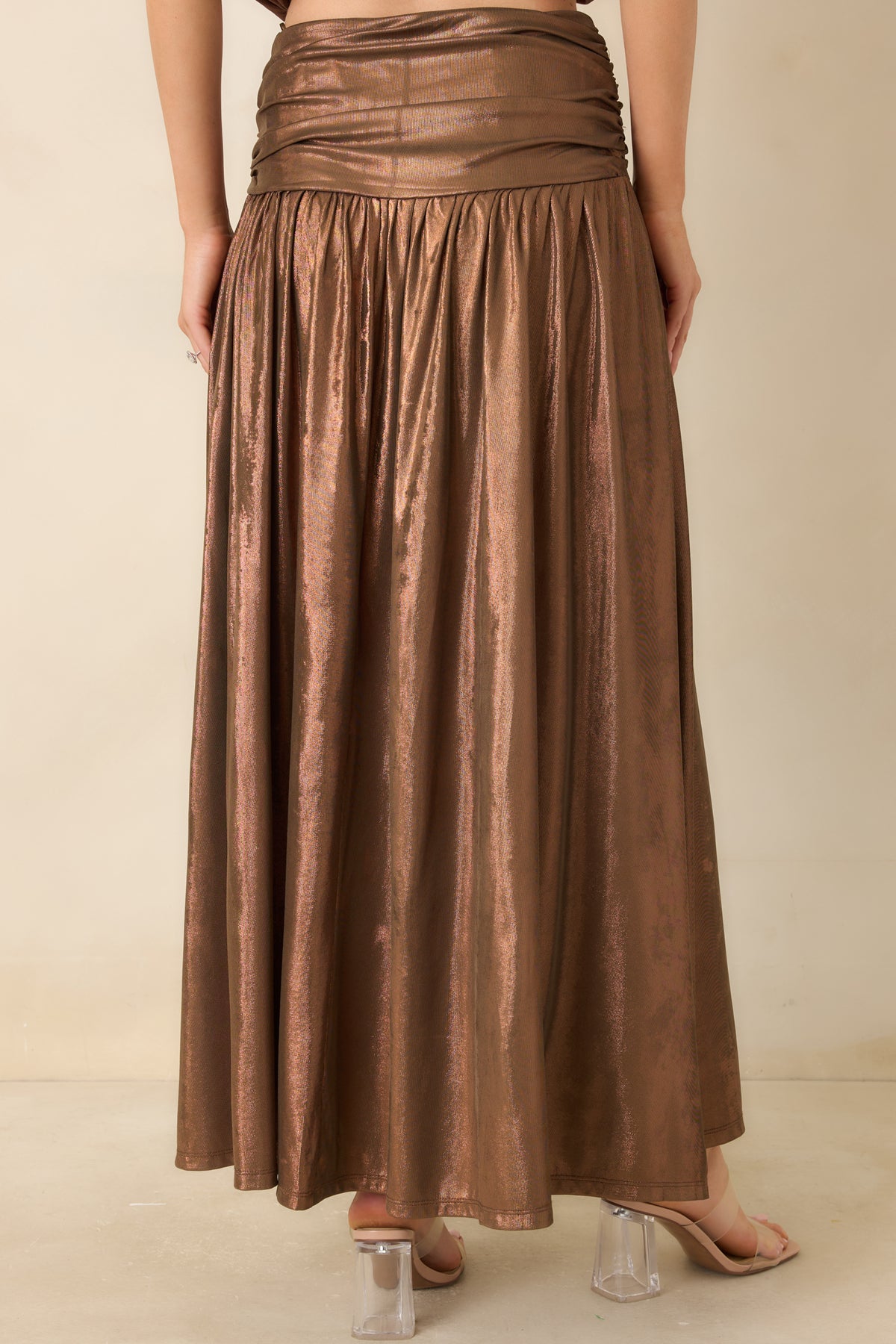 Rear of the bronze maxi skirt showing the concealed back zipper, wide ruched waistband, and flowing gathered skirt.