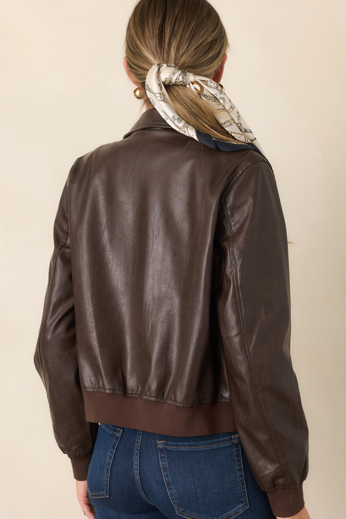 Rear view of the brown faux leather bomber jacket showing the smooth finish, ribbed knit hem, and gently gathered silhouette.