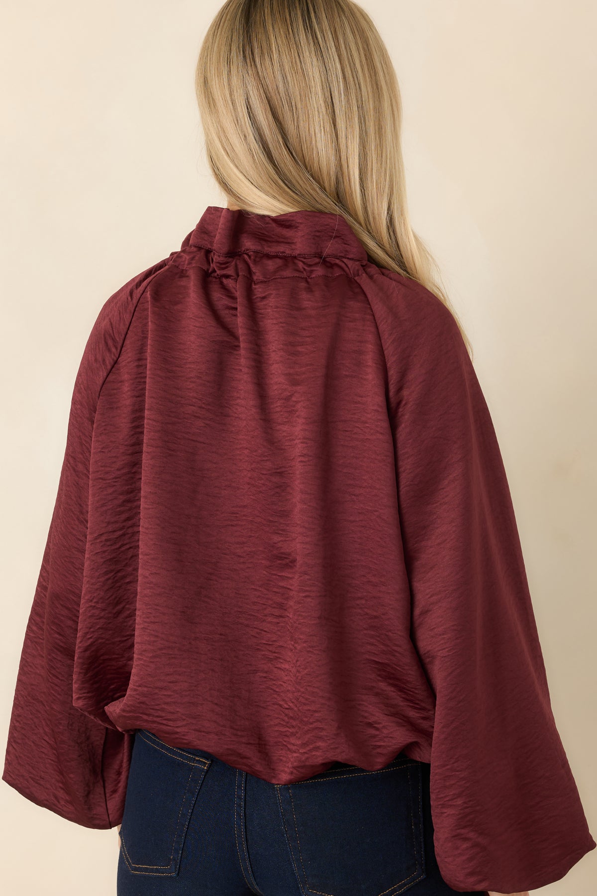 Rear of the burgundy blouse showing its softly crinkled fabric, voluminous long sleeves, and elasticized bubble hem.