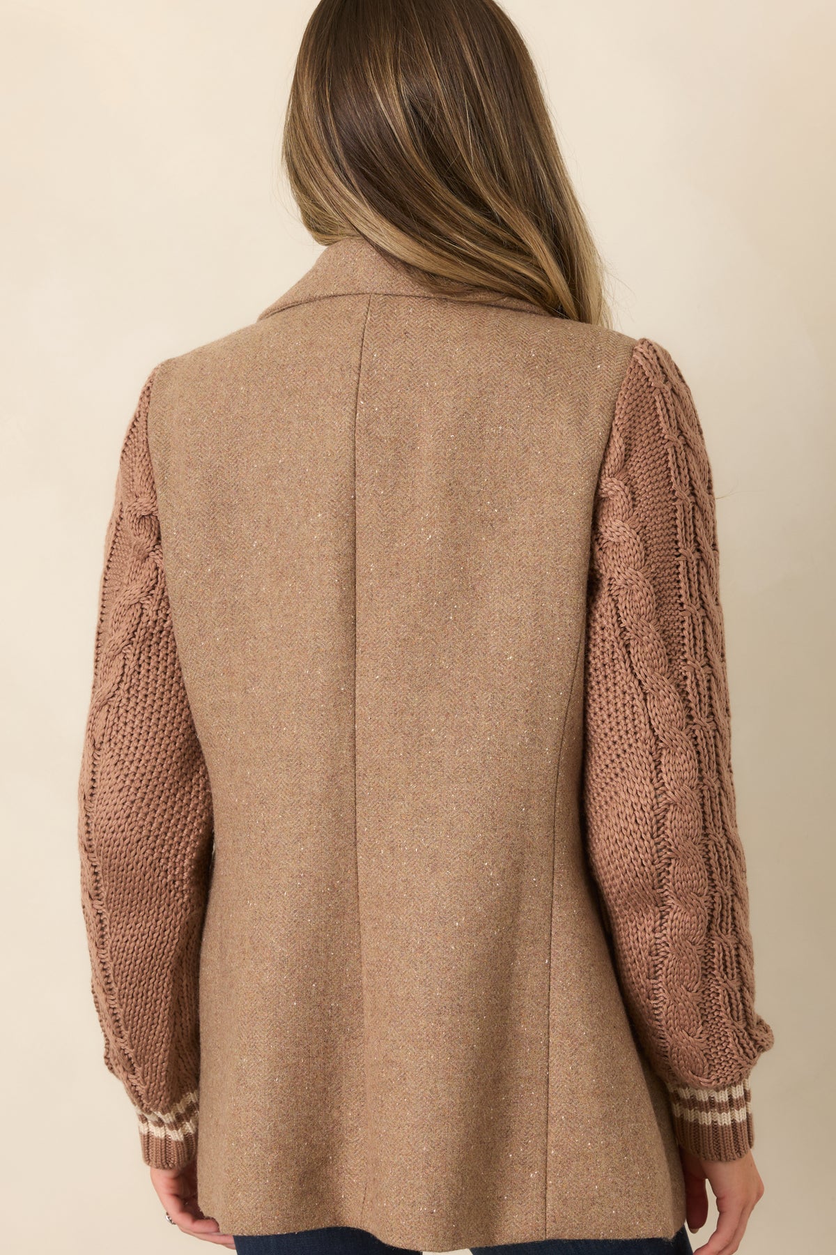 Rear view of the camel blazer showing its mid-thigh length, structured body, and contrasting cable-knit sleeves.