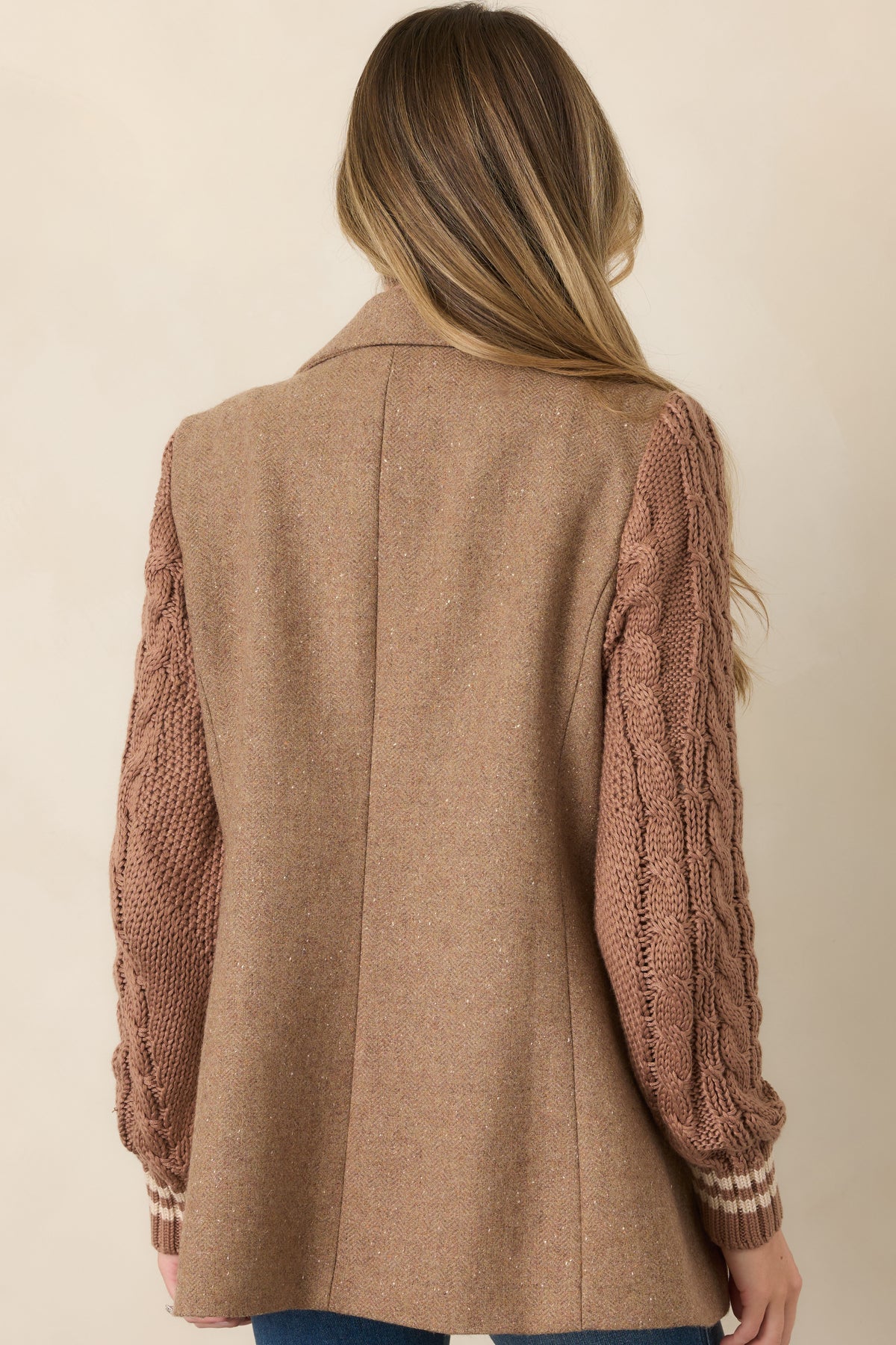 Rear view of the camel wool-blend blazer featuring a structured mid-thigh silhouette and contrasting cable-knit sleeves with ribbed cuffs.