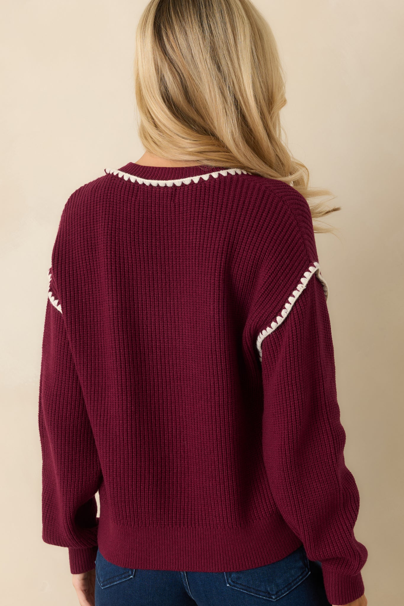 The back of the cardigan shows the ribbed knit construction and smooth maroon fabric with white whipstitch trim continuing along the hemline and sleeves.