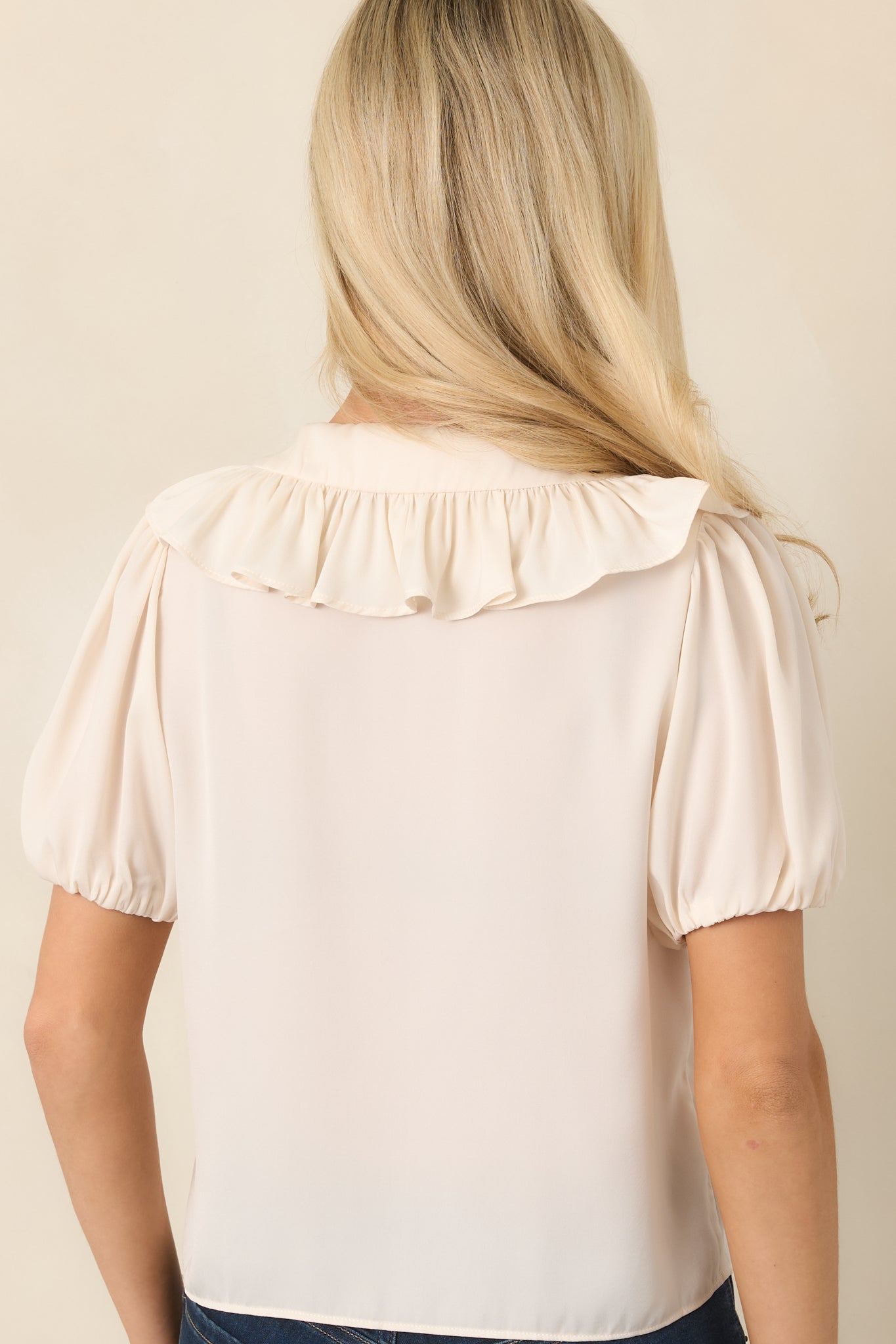 Rear view of the champagne cropped blouse showcasing its softly gathered shape, short puff sleeves, elasticized cuffs, and relaxed cropped hem.