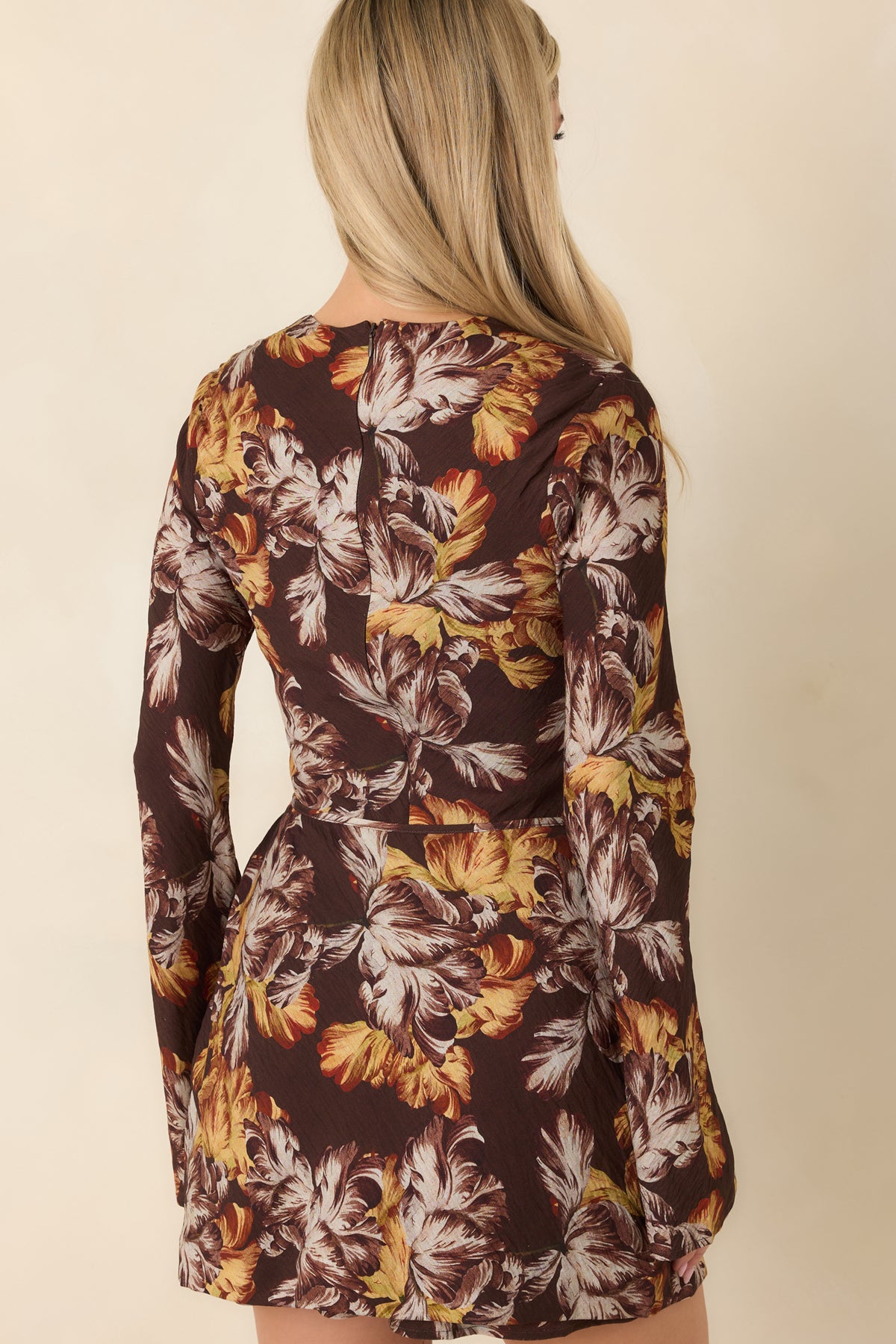 Rear view of the chocolate brown floral mini dress featuring a fitted bodice, long flared sleeves, and an oversized botanical print.