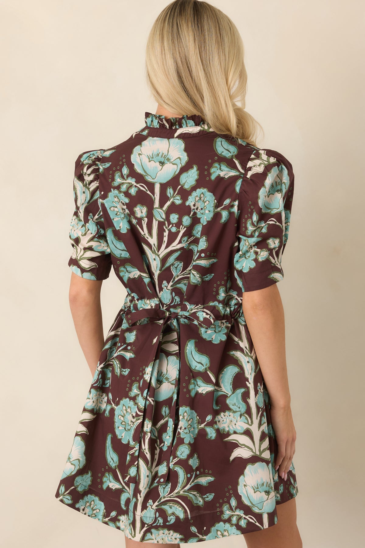 Rear view shows the chocolate brown floral print and waist tie defining the relaxed mini dress silhouette.