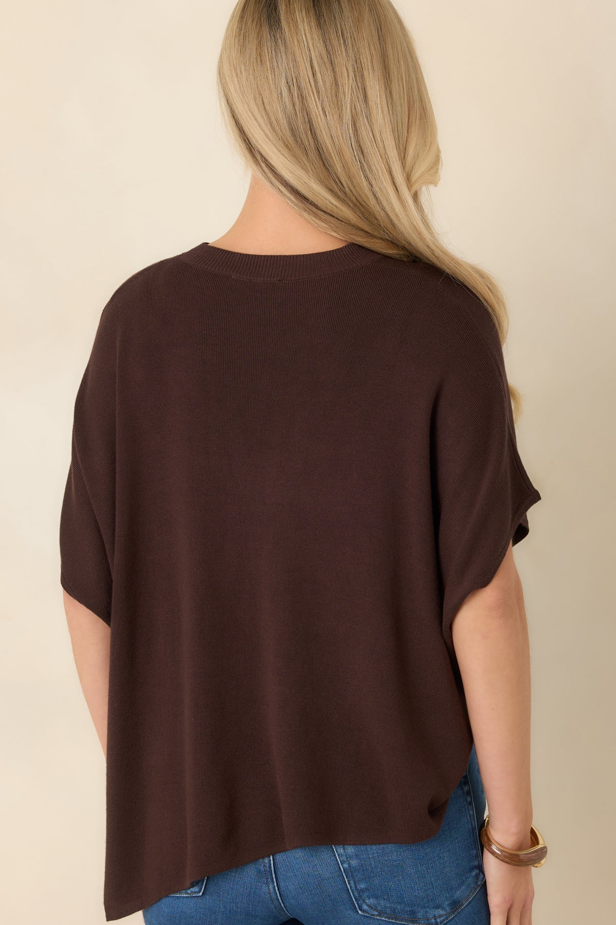 Rear of the chocolate brown knit top featuring a simple back, wide short sleeves, and an asymmetrical pointed hem.
