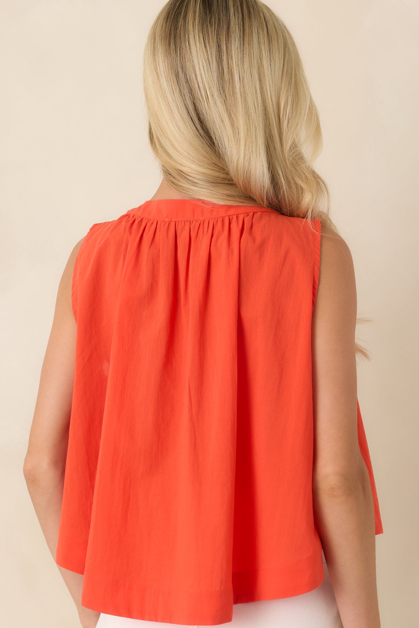 Rear view of the coral orange sleeveless cotton top highlighting the softly gathered neckline and relaxed flowing silhouette.