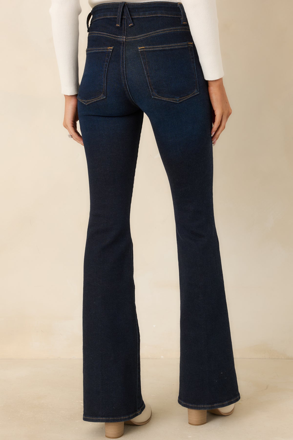 Rear of the deep indigo flared jeans featuring two back pockets, contrast stitching, belt loops, and finished hems.