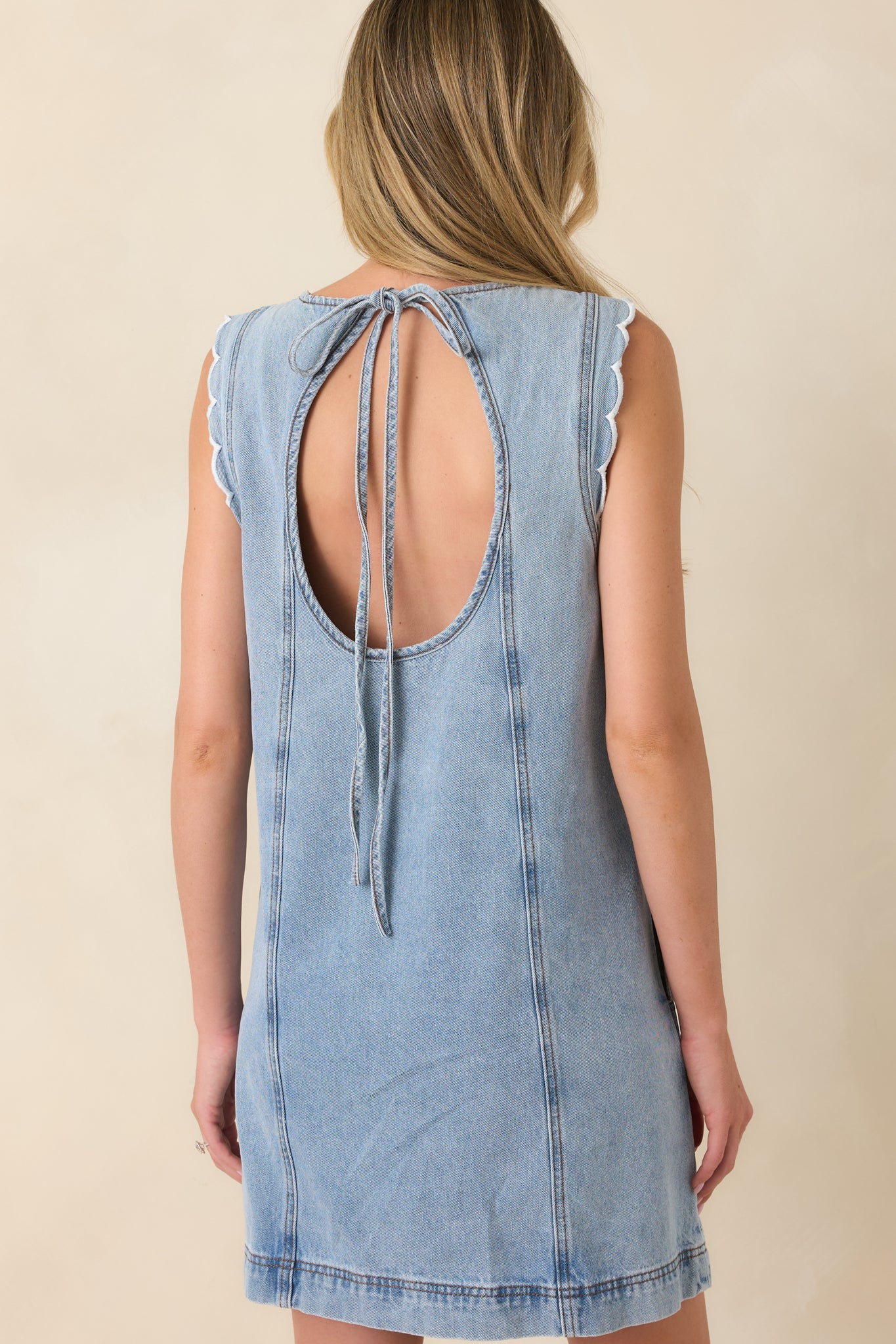 Rear view of the light vintage wash denim mini dress featuring an open back with an adjustable tie closure and a relaxed A-line silhouette.