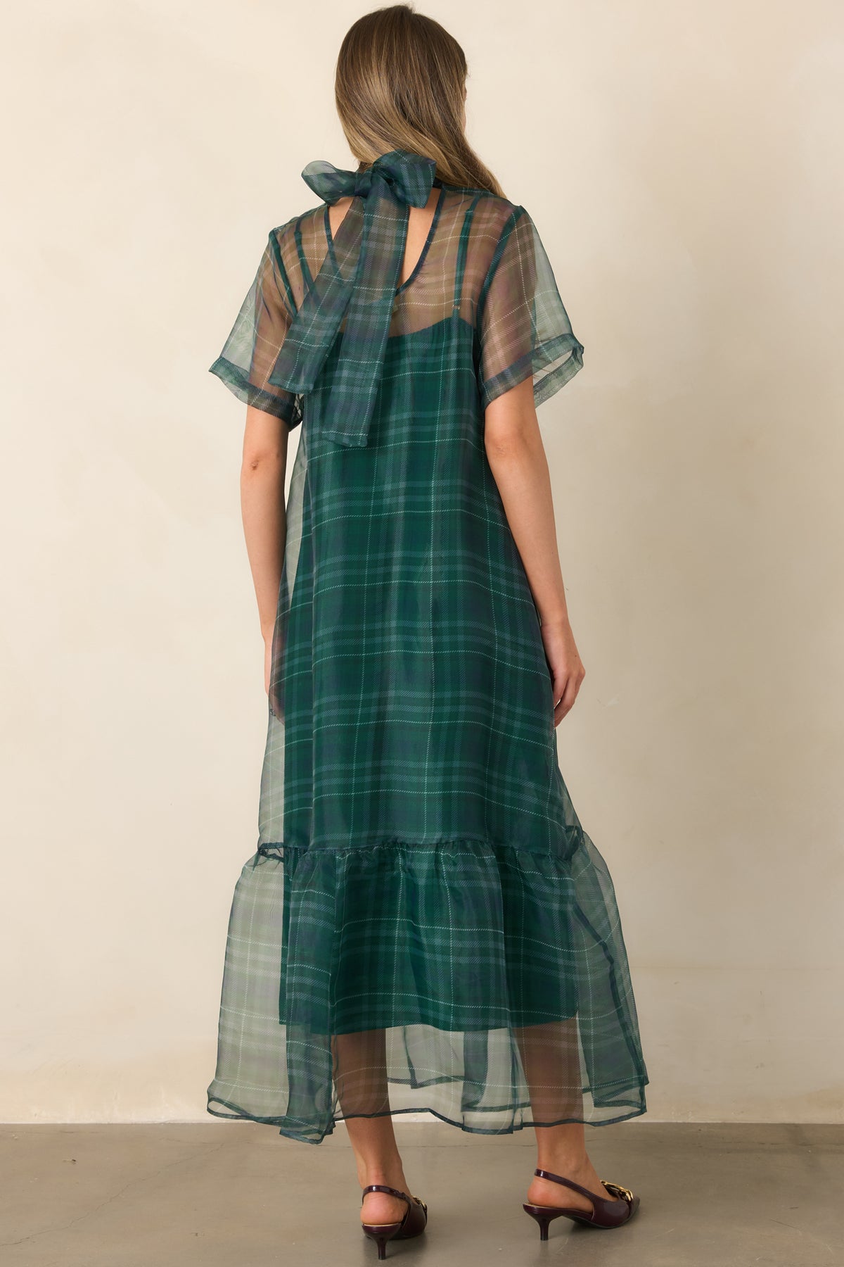 Rear of the emerald maxi dress showing the statement bow neckline, sheer sleeves, and gathered flounce hem.