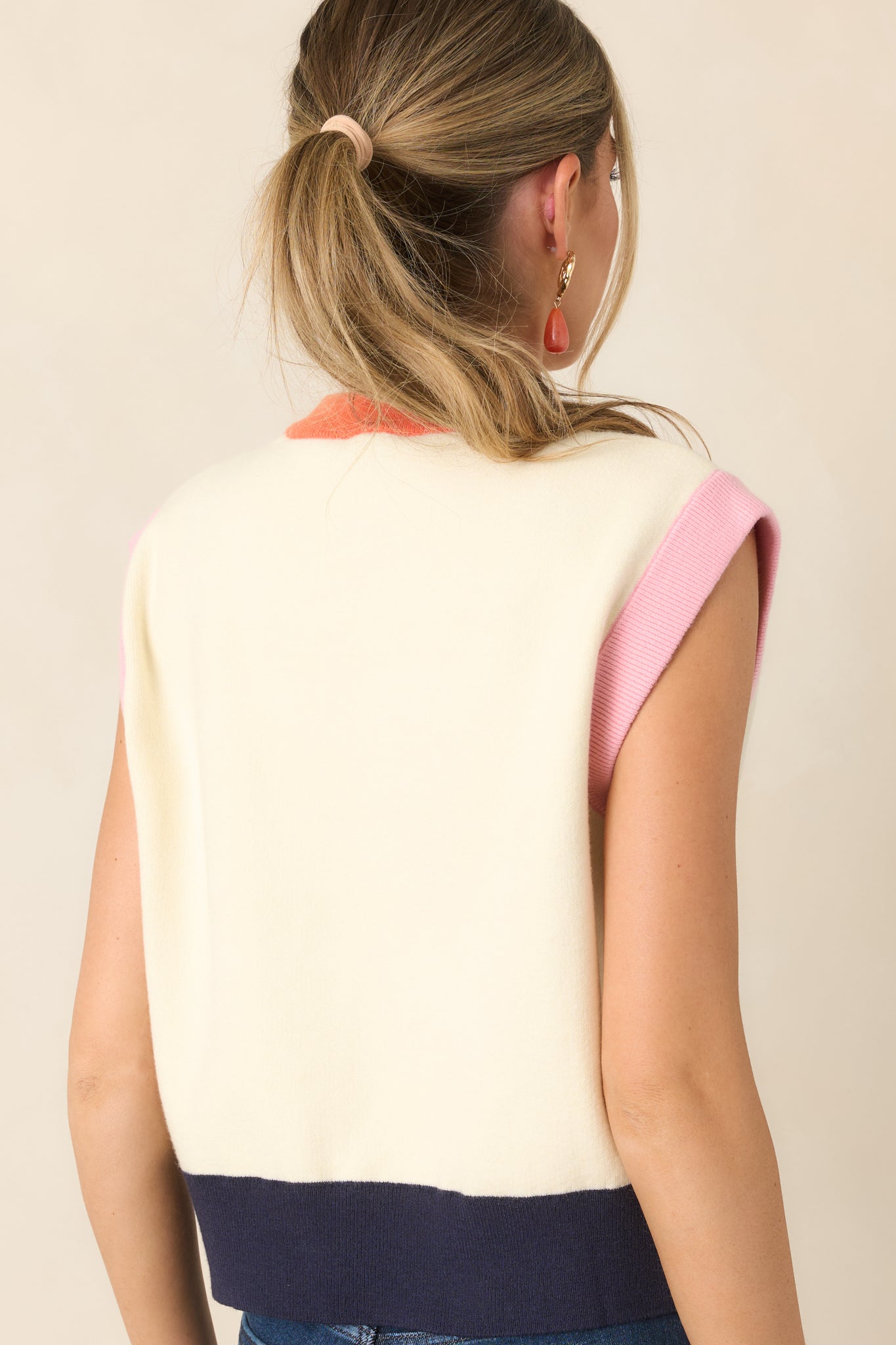 Rear view of the ivory sleeveless top showcasing the relaxed silhouette, orange neckline, soft pink armhole trim, and deep navy ribbed hem.