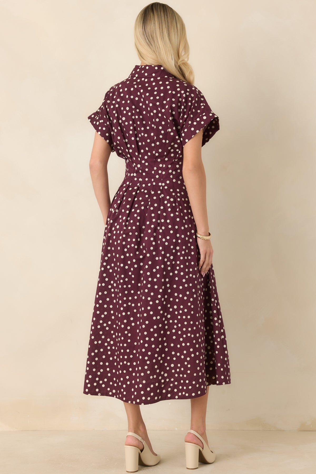  Rear view of the ivory cotton midi dress showing the short sleeves, tailored waist seams, plum polka dot pattern, and flowing skirt.