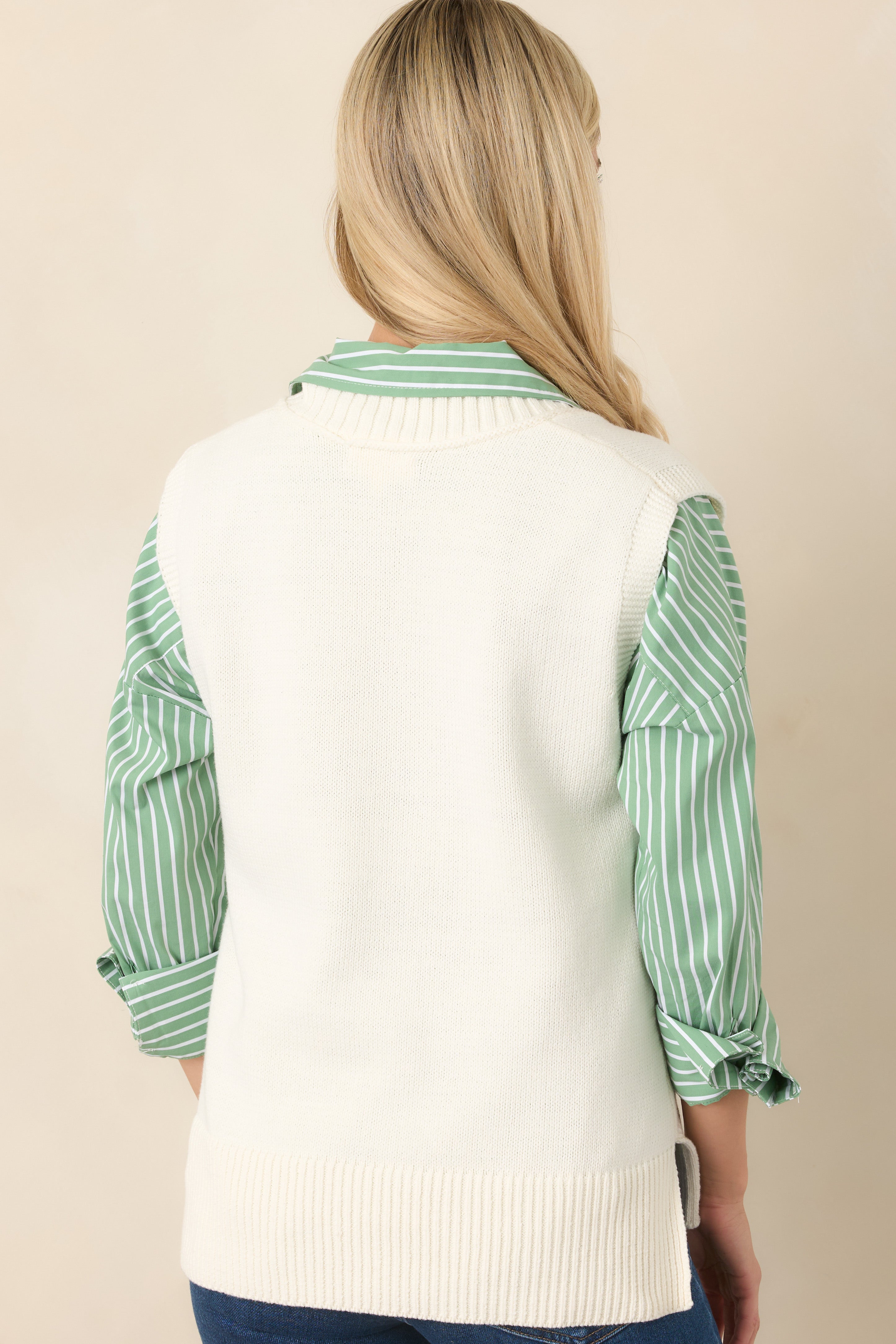 Rear view of the ivory knit sweater vest featuring a sleeveless silhouette, smooth knit body, and wide ribbed hem.