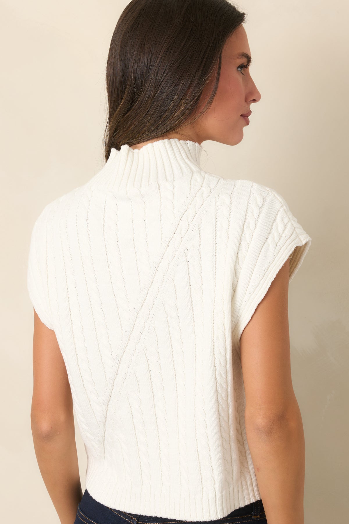 Rear of the ivory sleeveless sweater highlights the structured cable-knit pattern, relaxed silhouette, and ribbed hem.