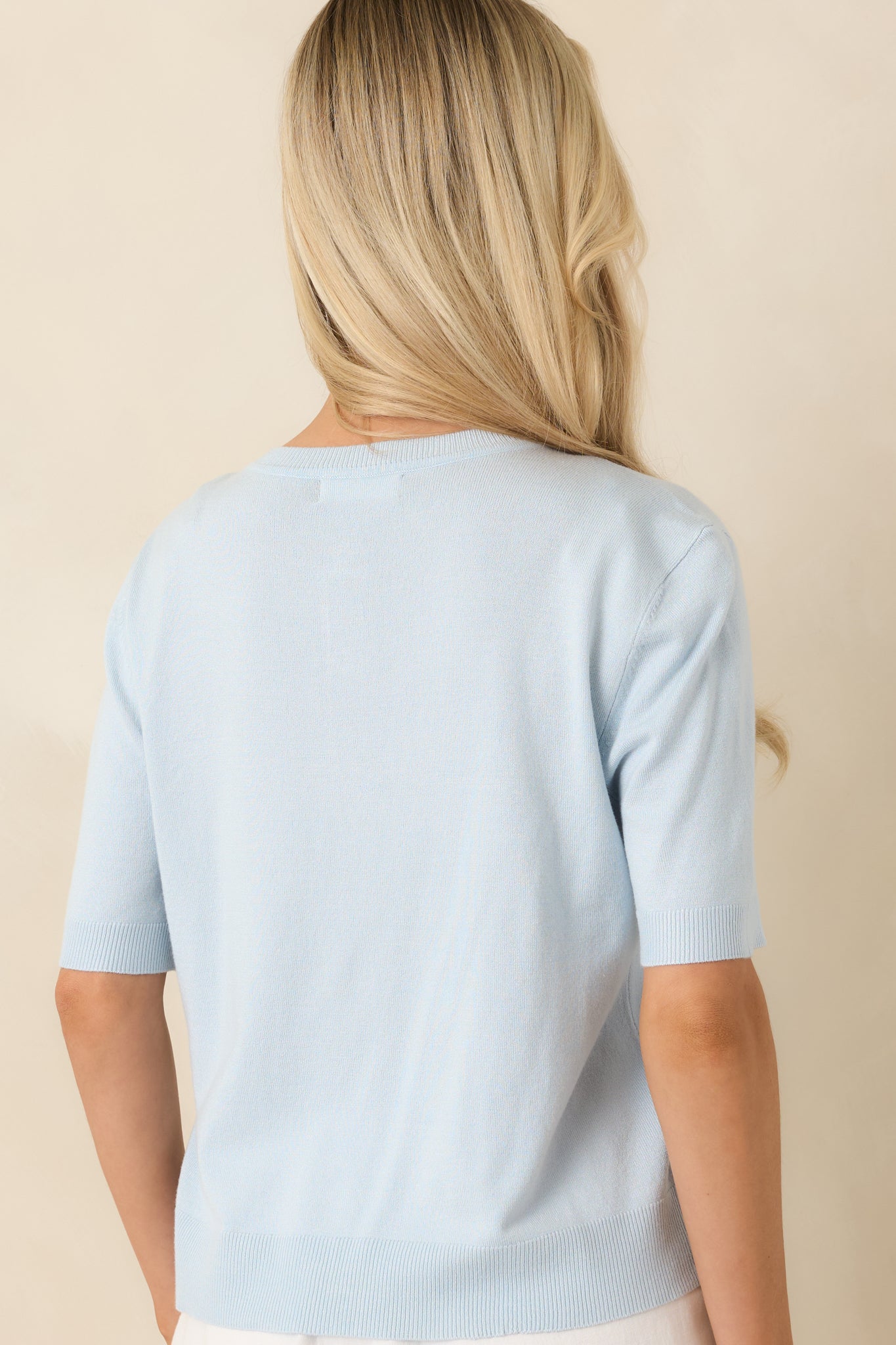Rear view of the light blue knit top highlighting the smooth knit fabric, short sleeves, and clean, minimalist finish.
