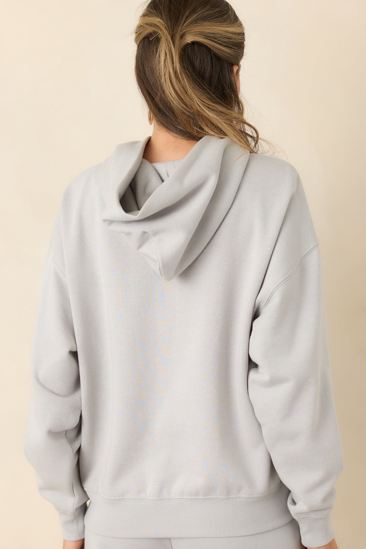 Rear of the light grey oversized hoodie featuring a roomy hood, dropped shoulders, and ribbed hem.