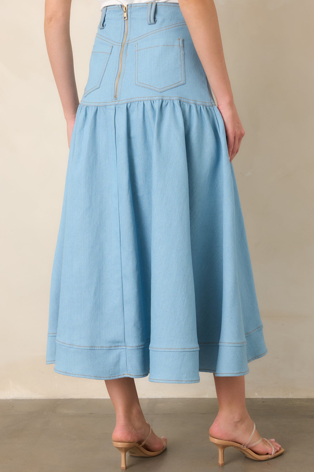Rear view of the light wash denim maxi skirt featuring back pockets, belt loops, a zipper closure, and a wide tiered hem.