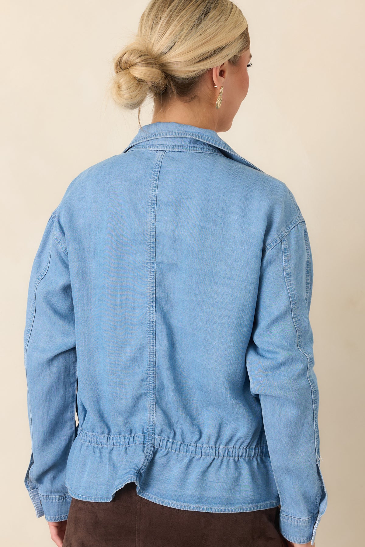 Rear of the medium wash denim top showing the relaxed fit, drawstring waist, and peplum hem.