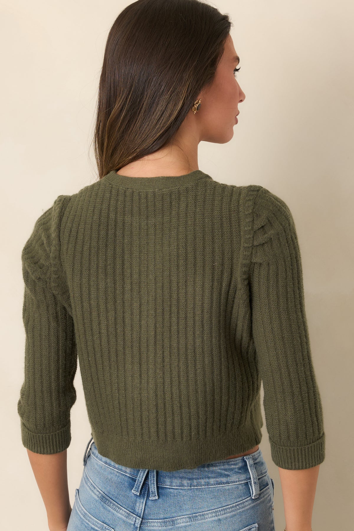 Rear of the moss green cardigan showing its vertical ribbing, gathered shoulders, and cropped silhouette.