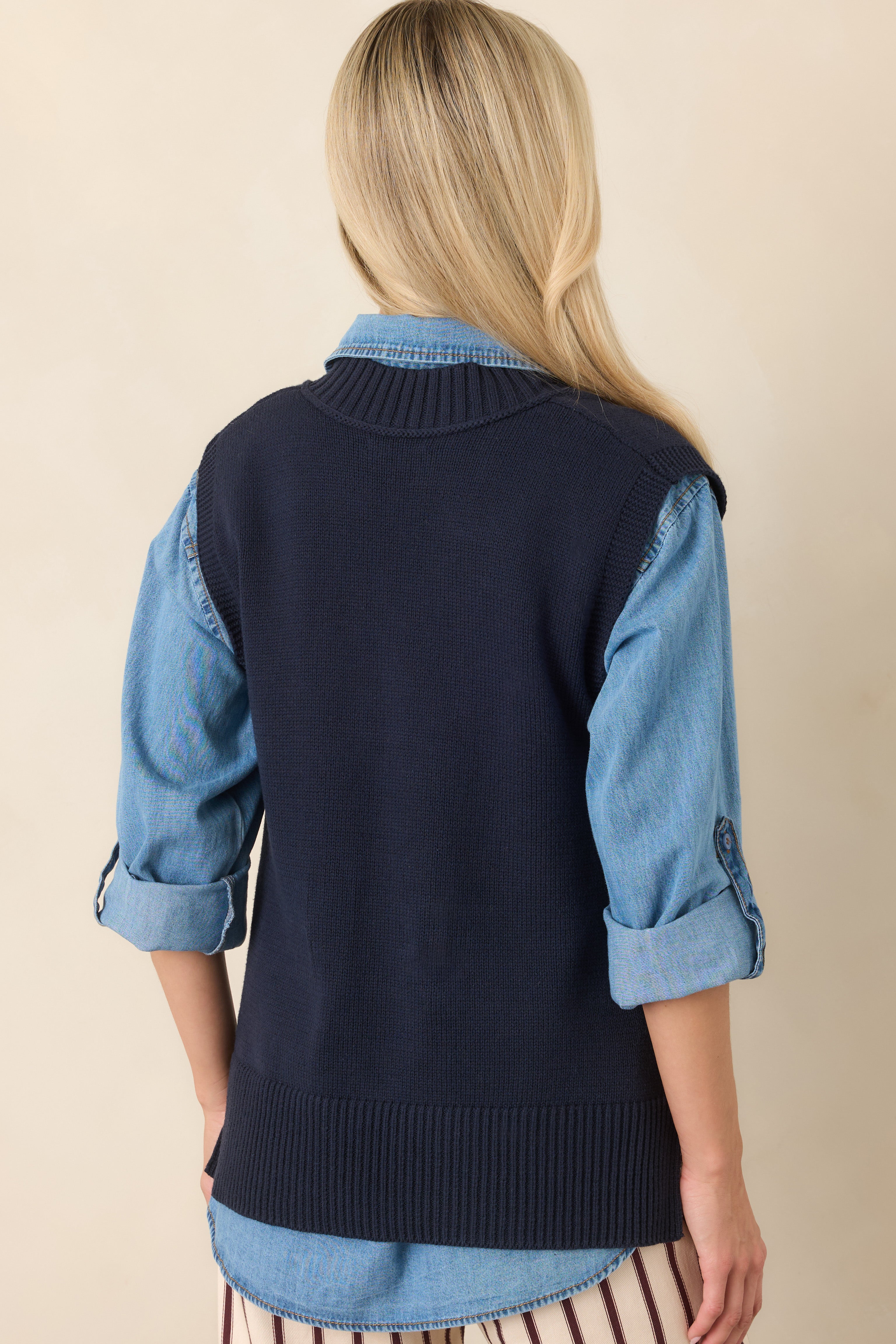 Rear view of the navy knit sweater vest featuring a sleeveless silhouette, smooth knit body, and wide ribbed hem.
