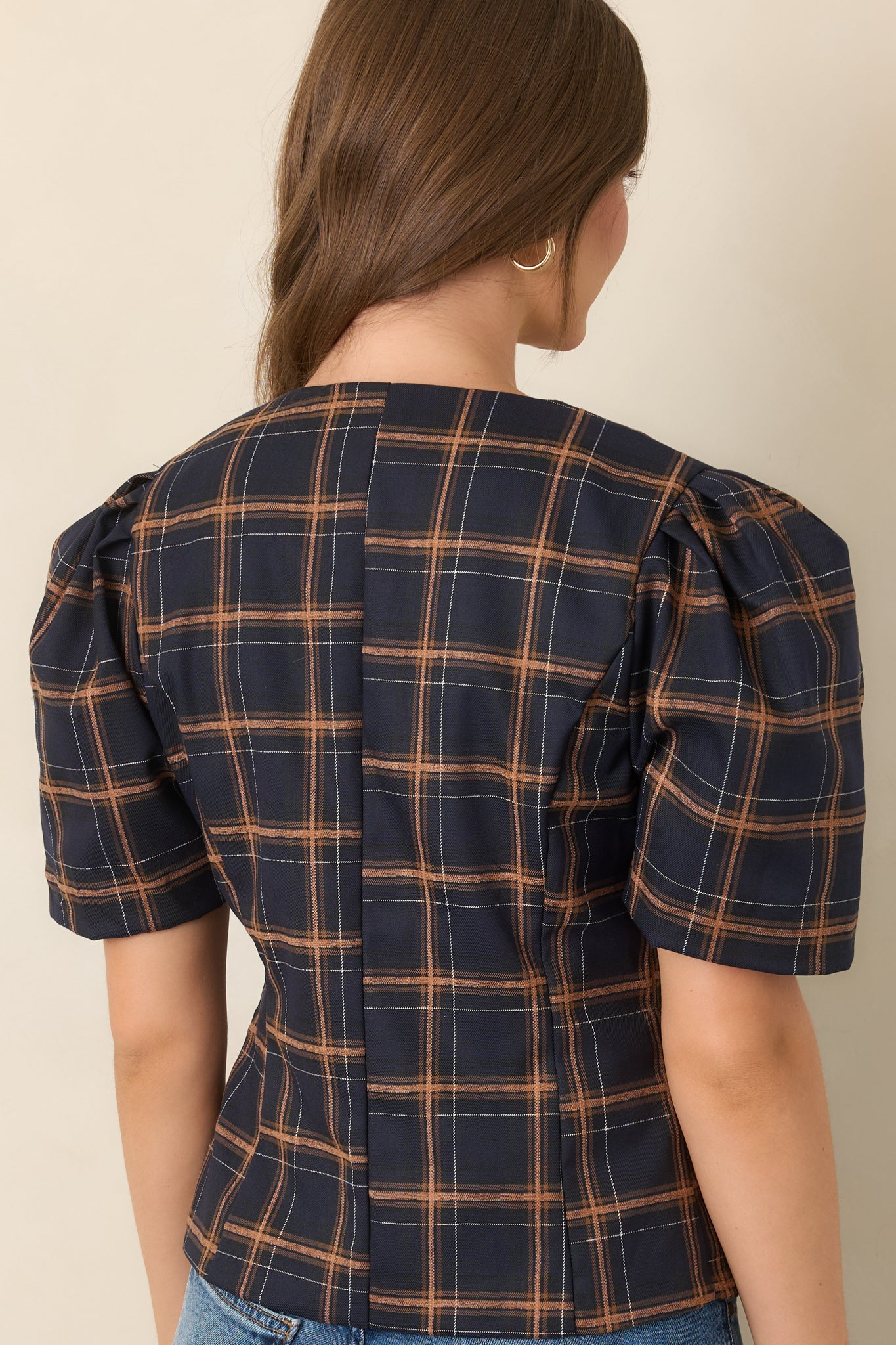 Rear view of the structured plaid top highlighting its navy, camel, and ivory woven pattern, tailored seams, fitted waist, and voluminous elbow-length sleeves.