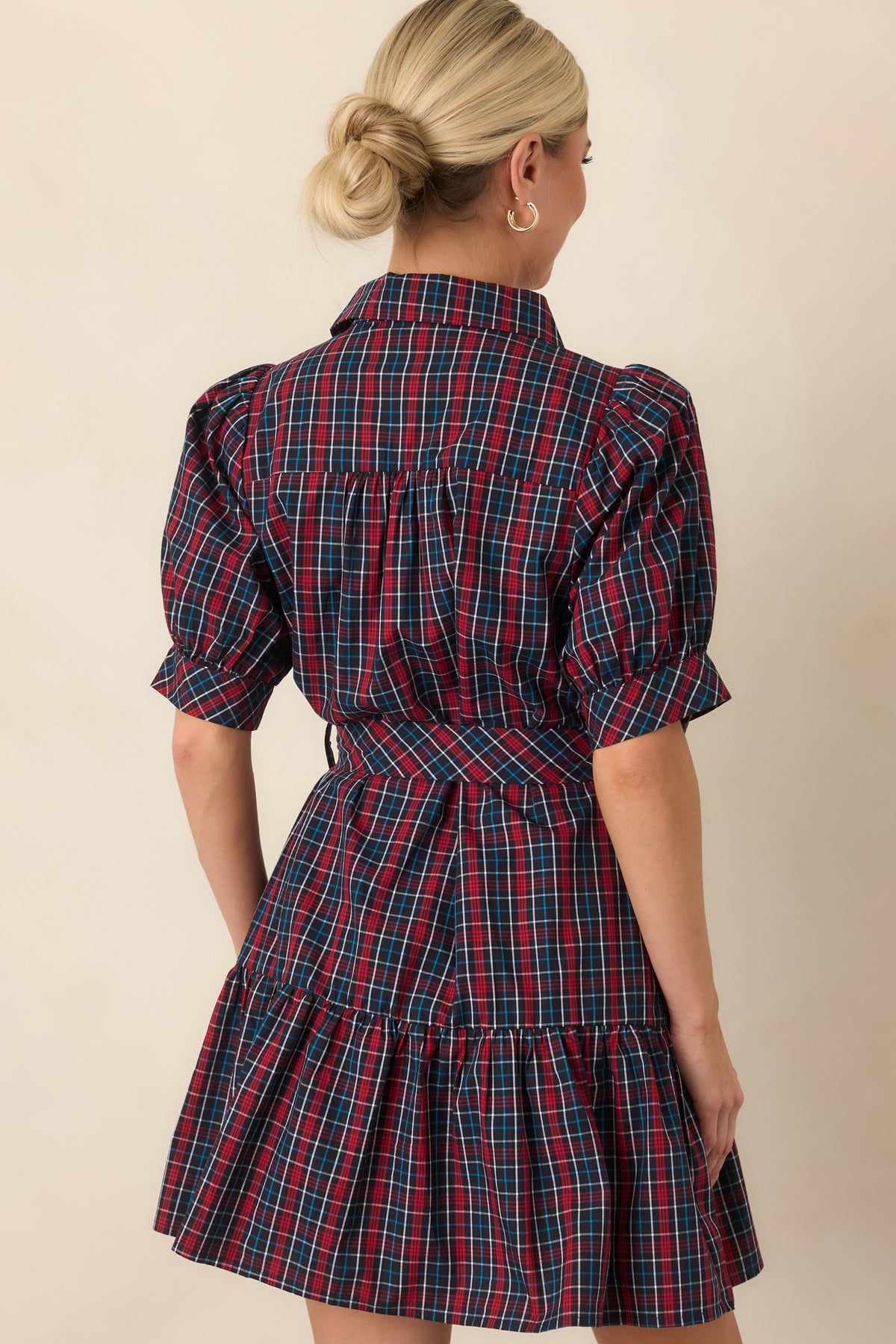 Rear view of the navy and red plaid mini dress showing its relaxed bodice, matching waist belt, and tiered skirt.