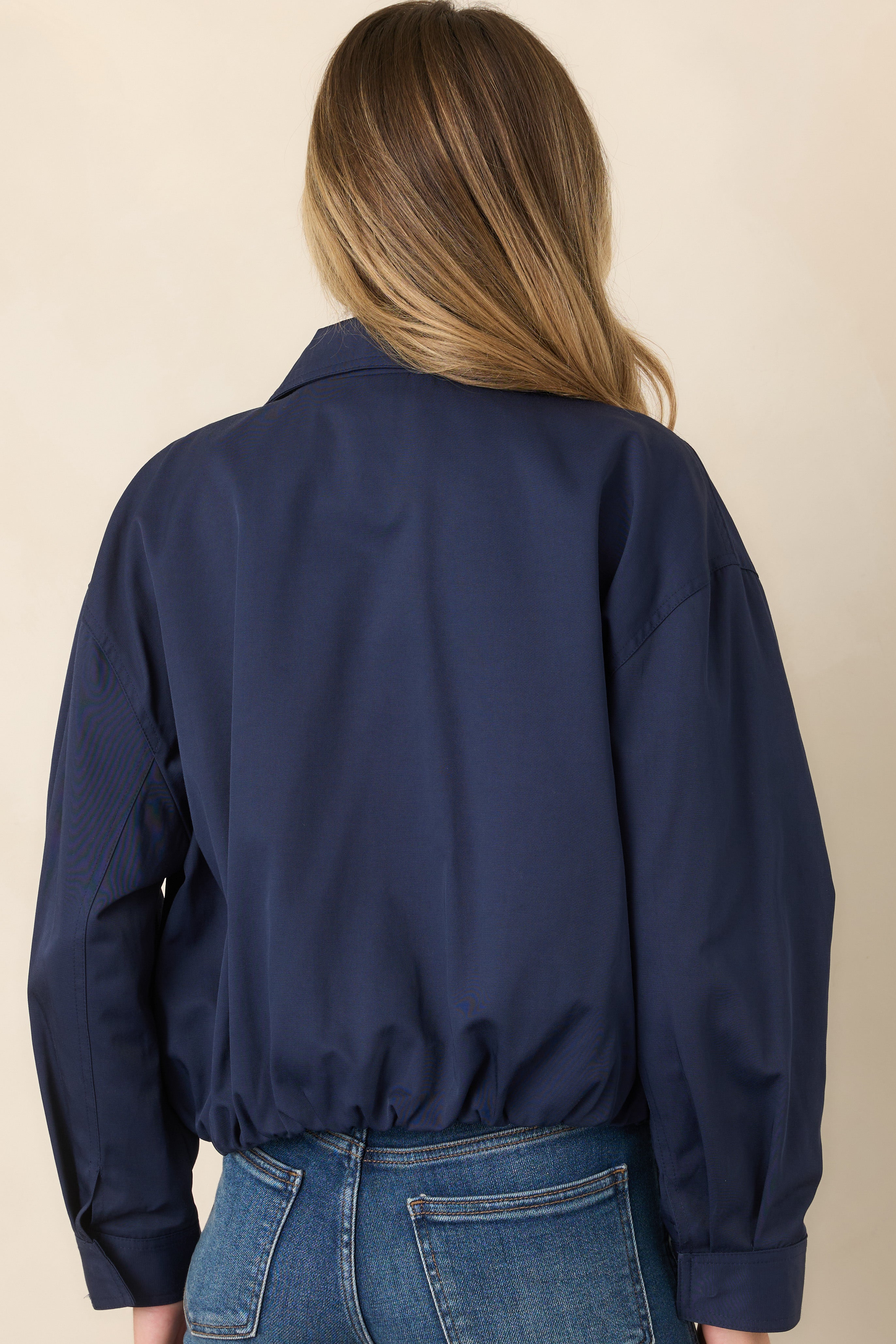 Rear view of the navy bomber jacket featuring dropped shoulders, long sleeves, a relaxed cropped silhouette, and elasticized back hem.
