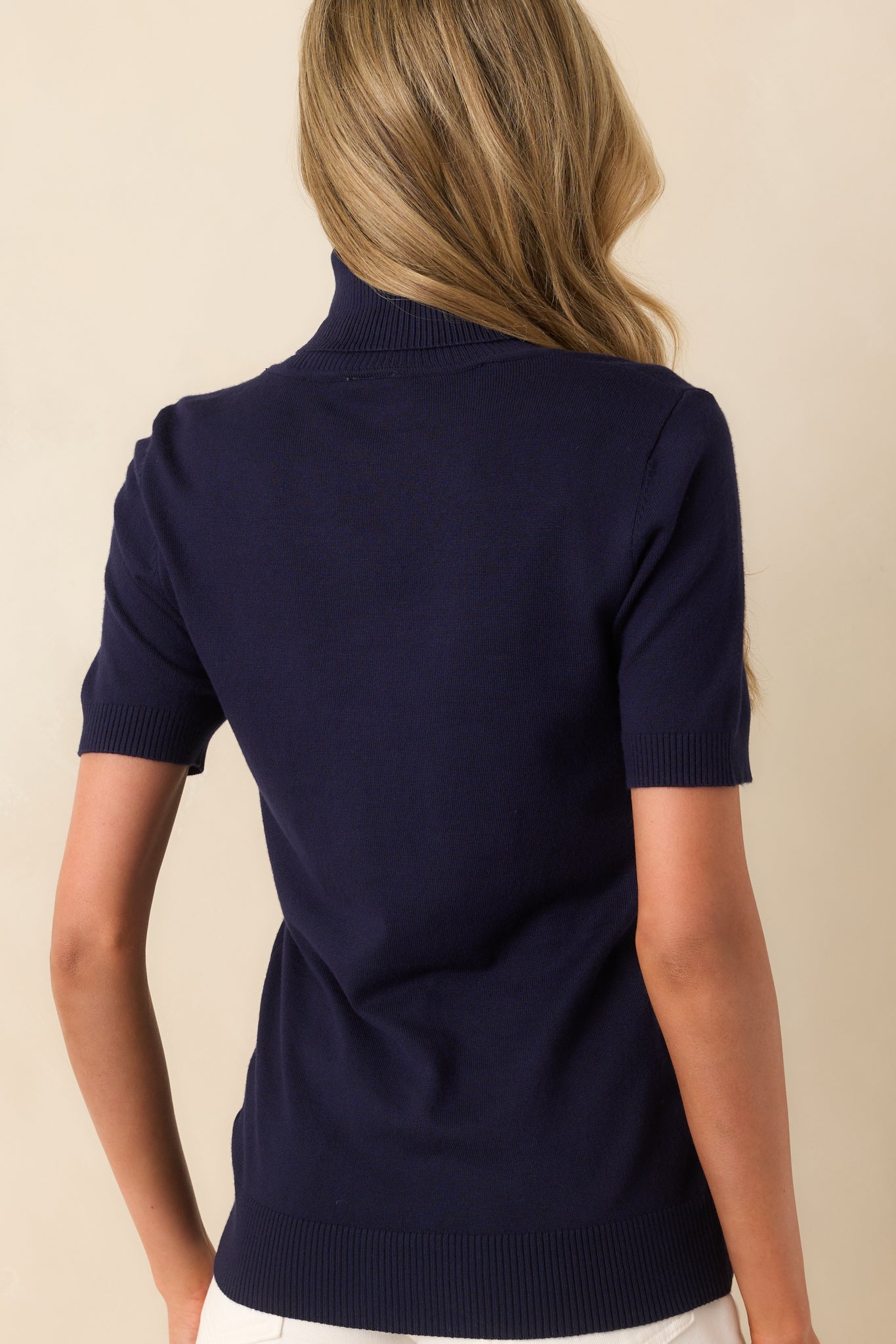 A view from behind of the navy sweater, displaying the fitted back silhouette and the continuation of the ribbed knit fabric.