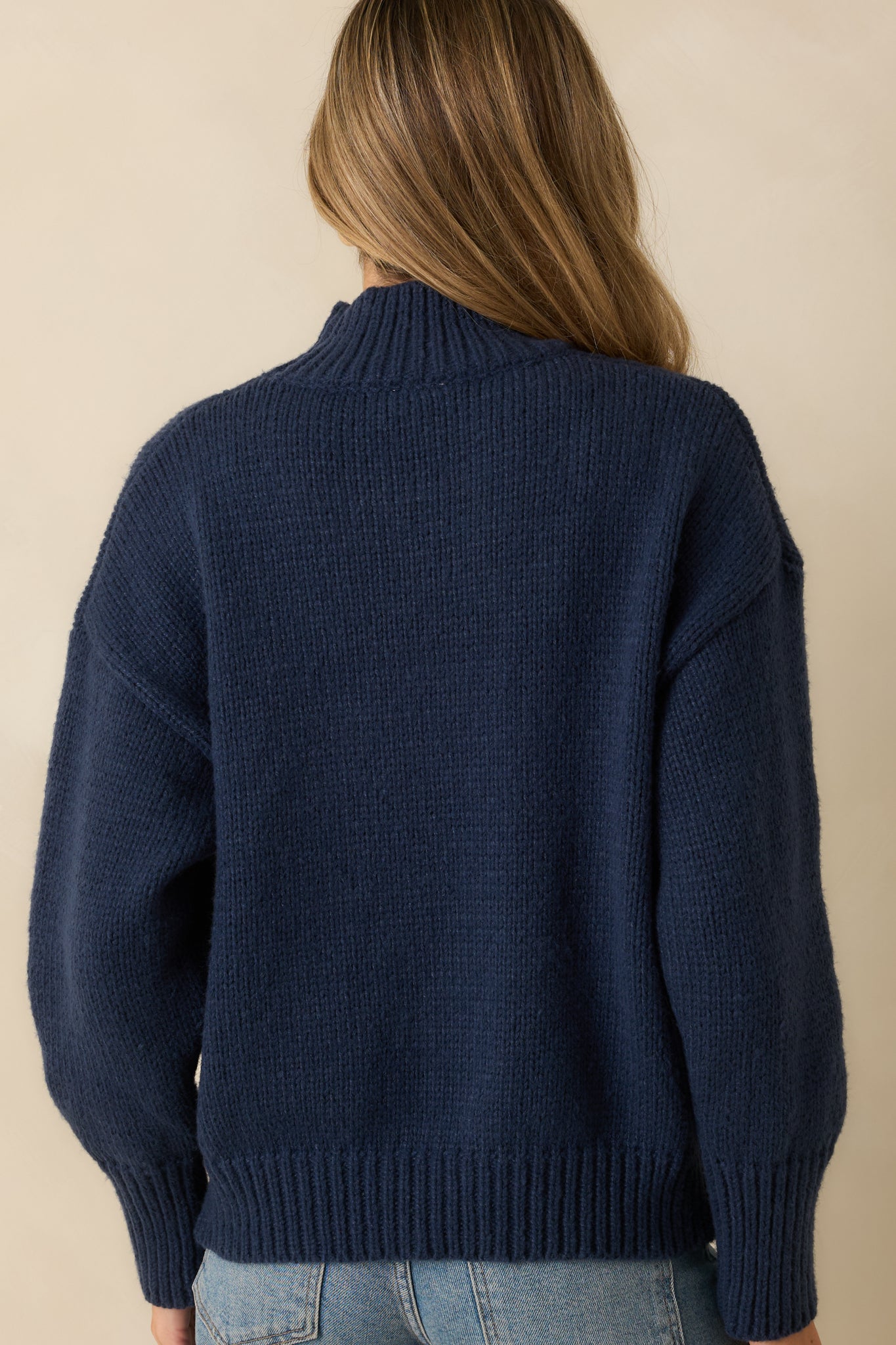 Back view of the navy turtleneck sweater displaying the smooth knit surface, ribbed hem and cuffs, and relaxed silhouette.