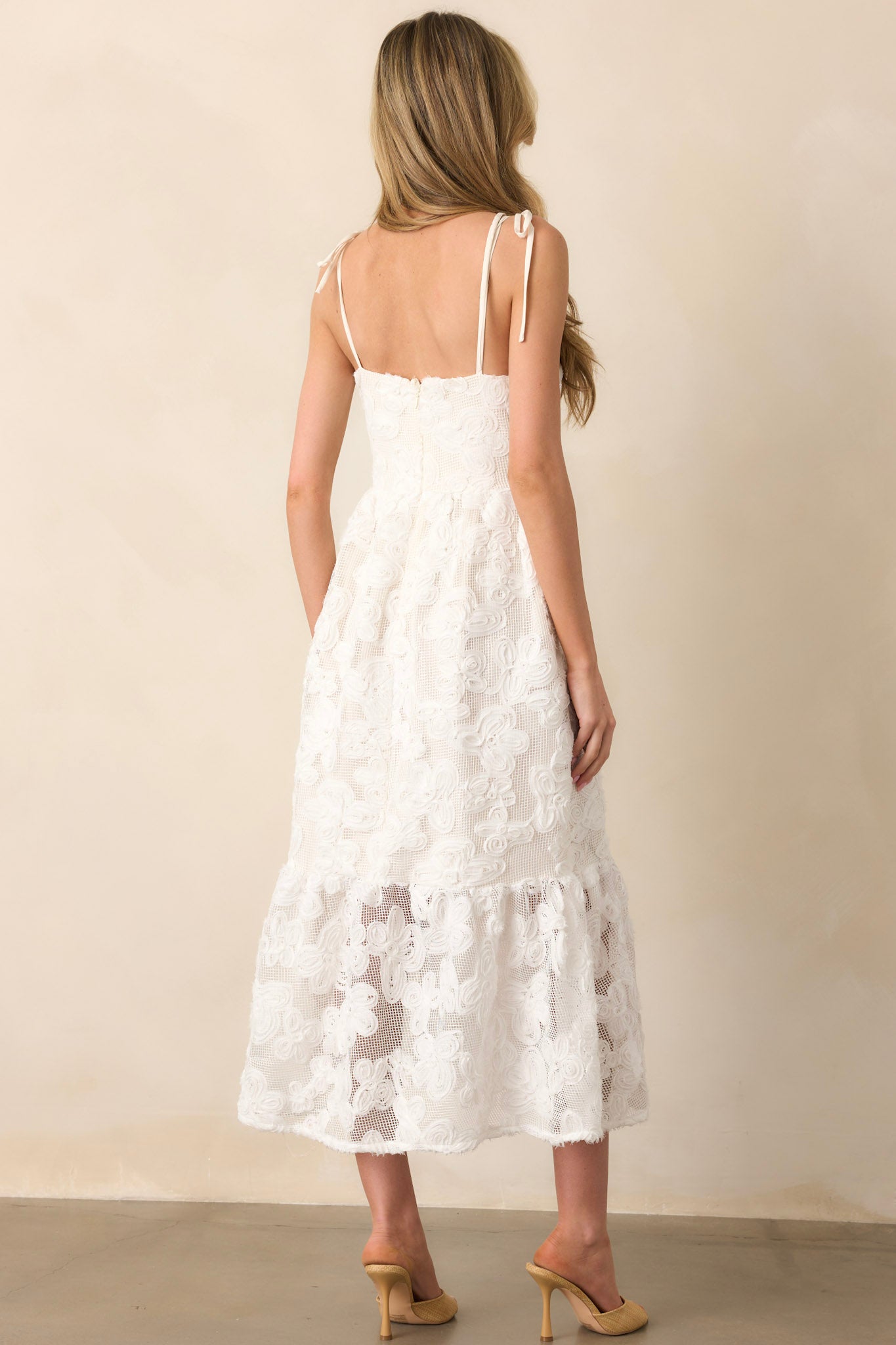 The rear of a maxi dress featuring a hidden zipper, self-tie bow straps, and a smocked panel for a comfortable fit. The lace overlay continues for a cohesive, elegant design.