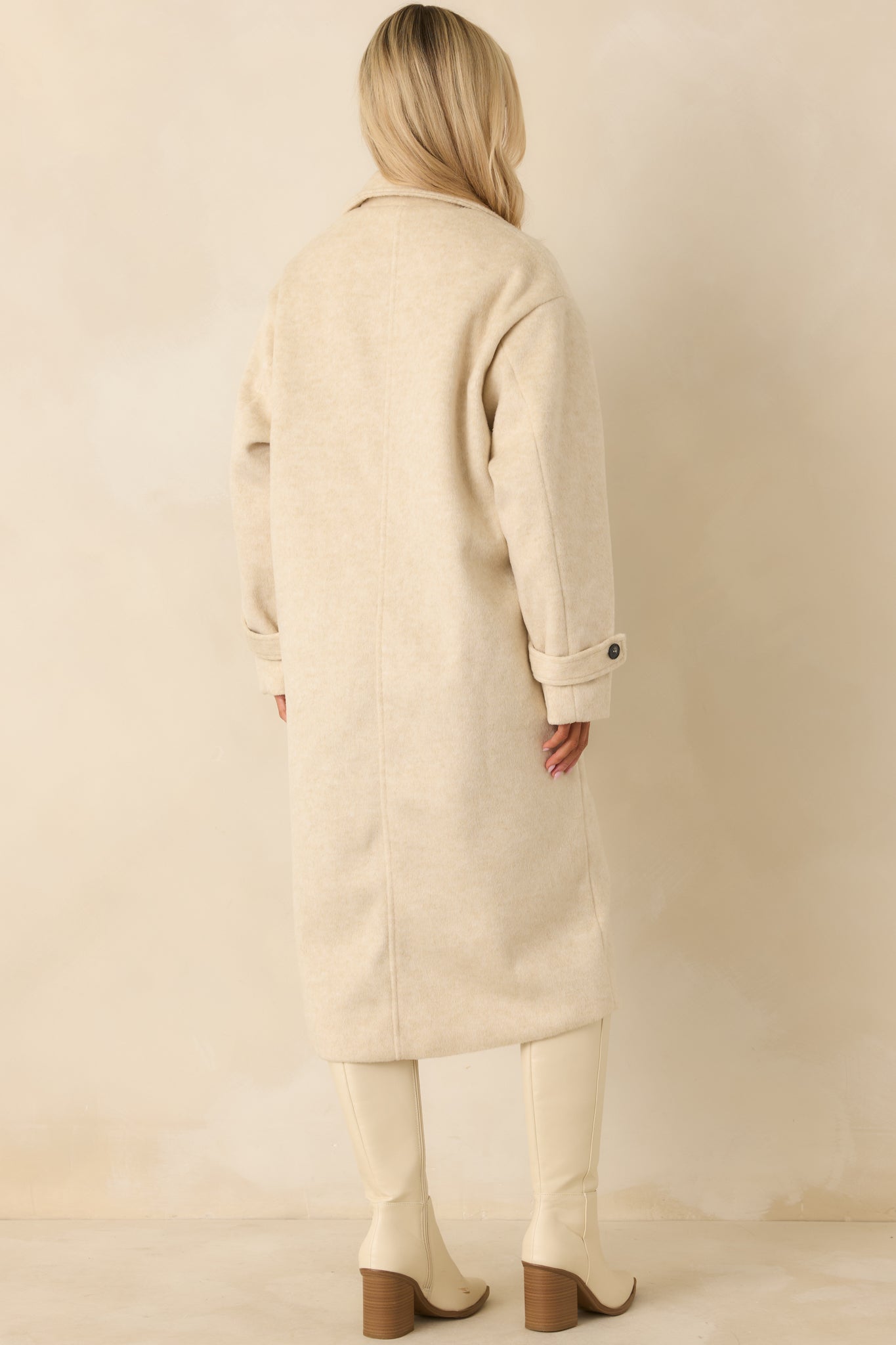 Rear of the ivory longline coat featuring a back belt detail, smooth wool-blend fabric, and relaxed fit across the shoulders and hem.