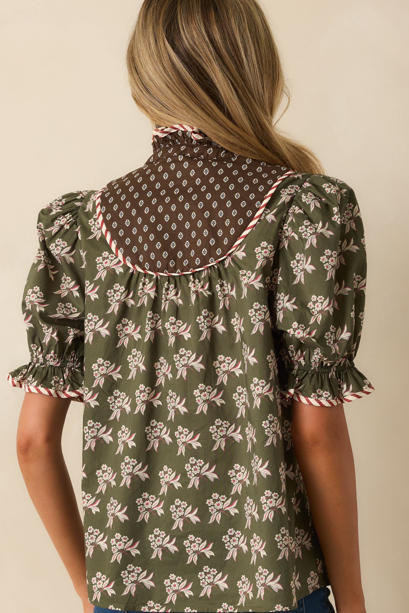 Rear view of the olive green floral top with puff sleeves, smocked cuffs, and piping trim.