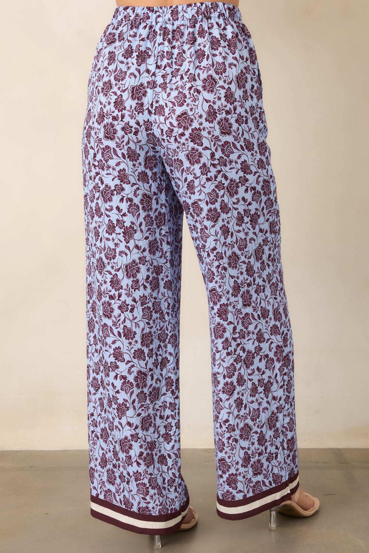 Rear view of the pale lilac pants showing the burgundy floral print, relaxed wide legs, and striped hems.