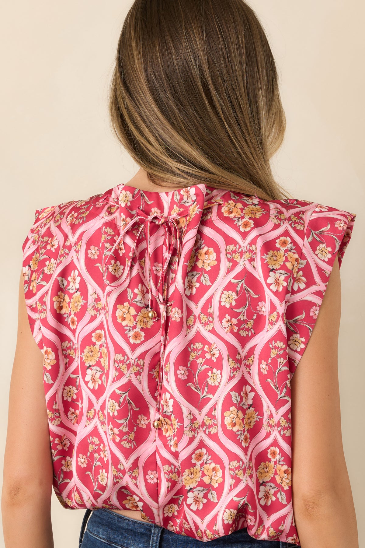 Rear of the pink floral top featuring a back-tied drawstring neckline with gold bead accents and a bubble hem.