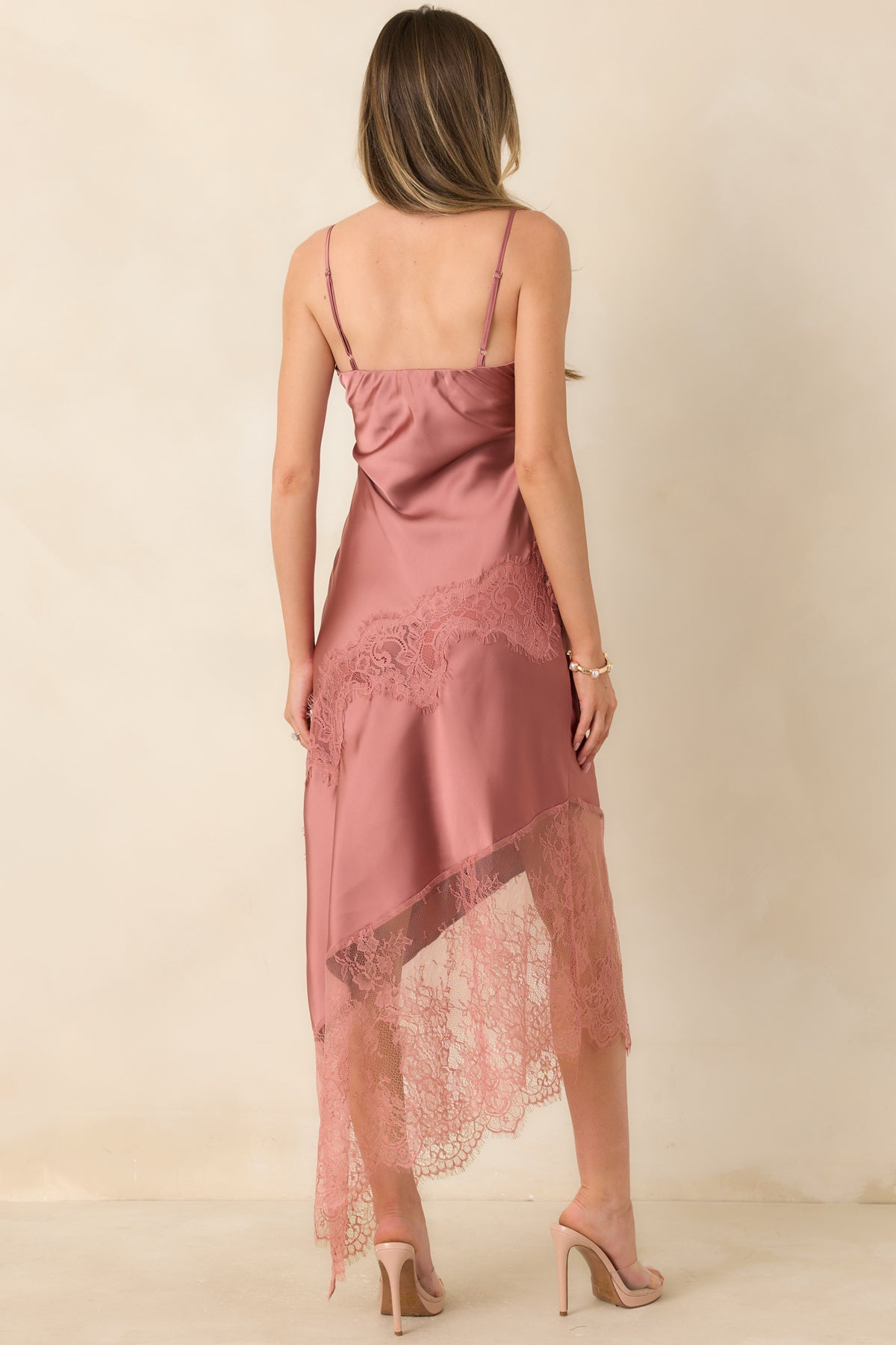 Rear of the rose pink satin slip dress featuring delicate spaghetti straps, smooth satin fabric, and an asymmetric lace-trimmed hem.