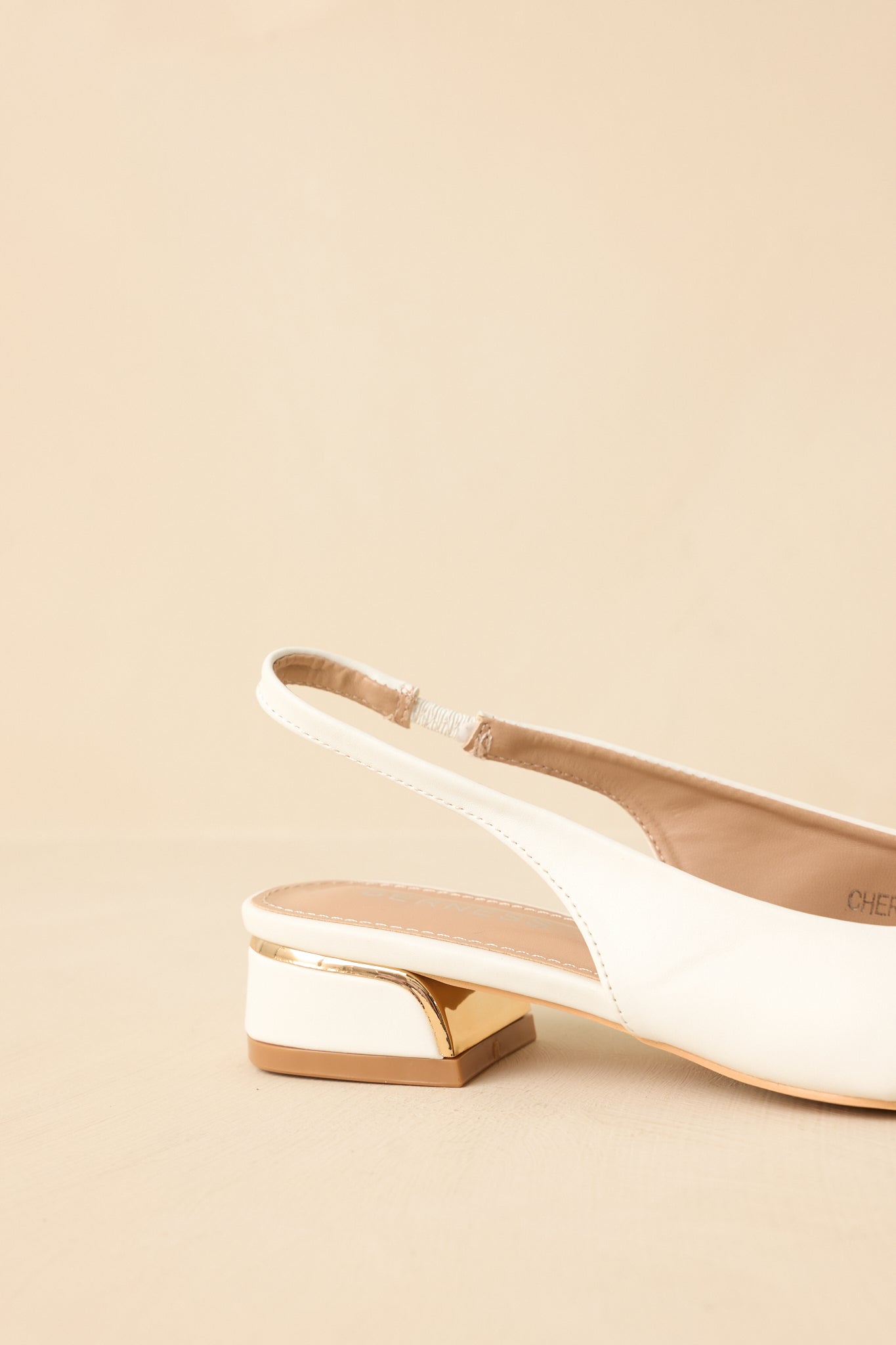 Angled rear-side view against a beige background focusing on the slingback strap and low-profile sole.